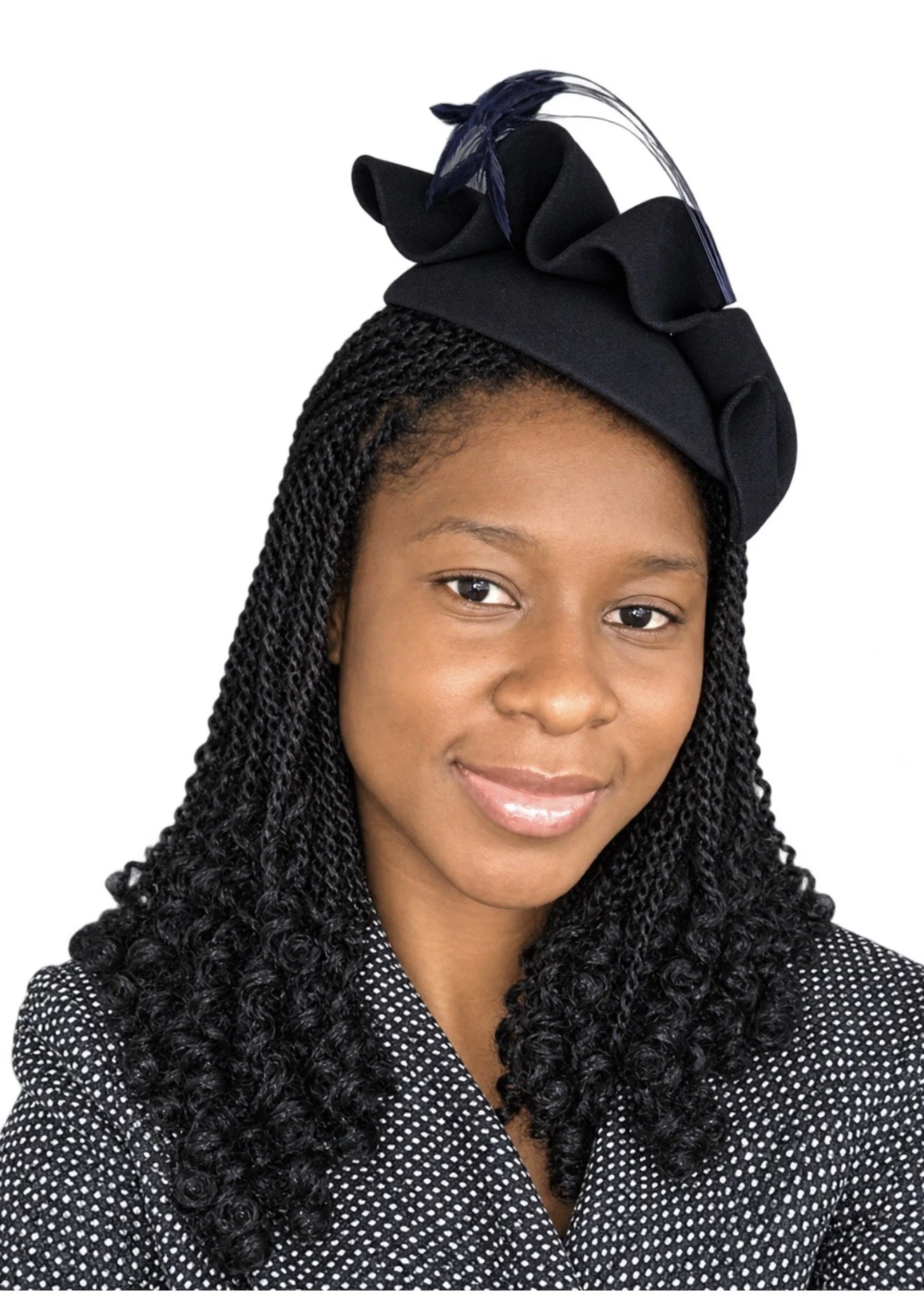 A woman with black braided hair wearing a black and white polka dot jacket and a black headwrap adorned with a black bow and feather.