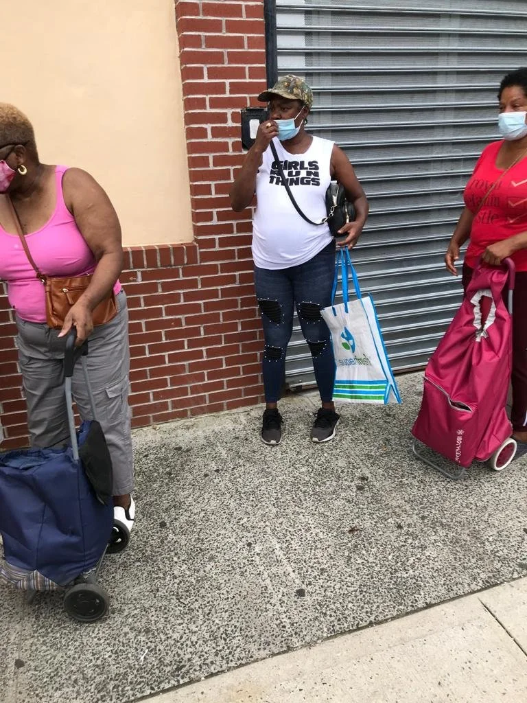 Three women standing outside, wearing face masks, with luggage and shopping bags.