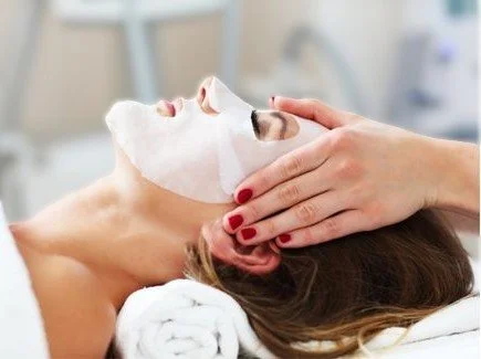 Woman receiving a facial treatment with a white mask applied to her face in a spa or clinic setting.