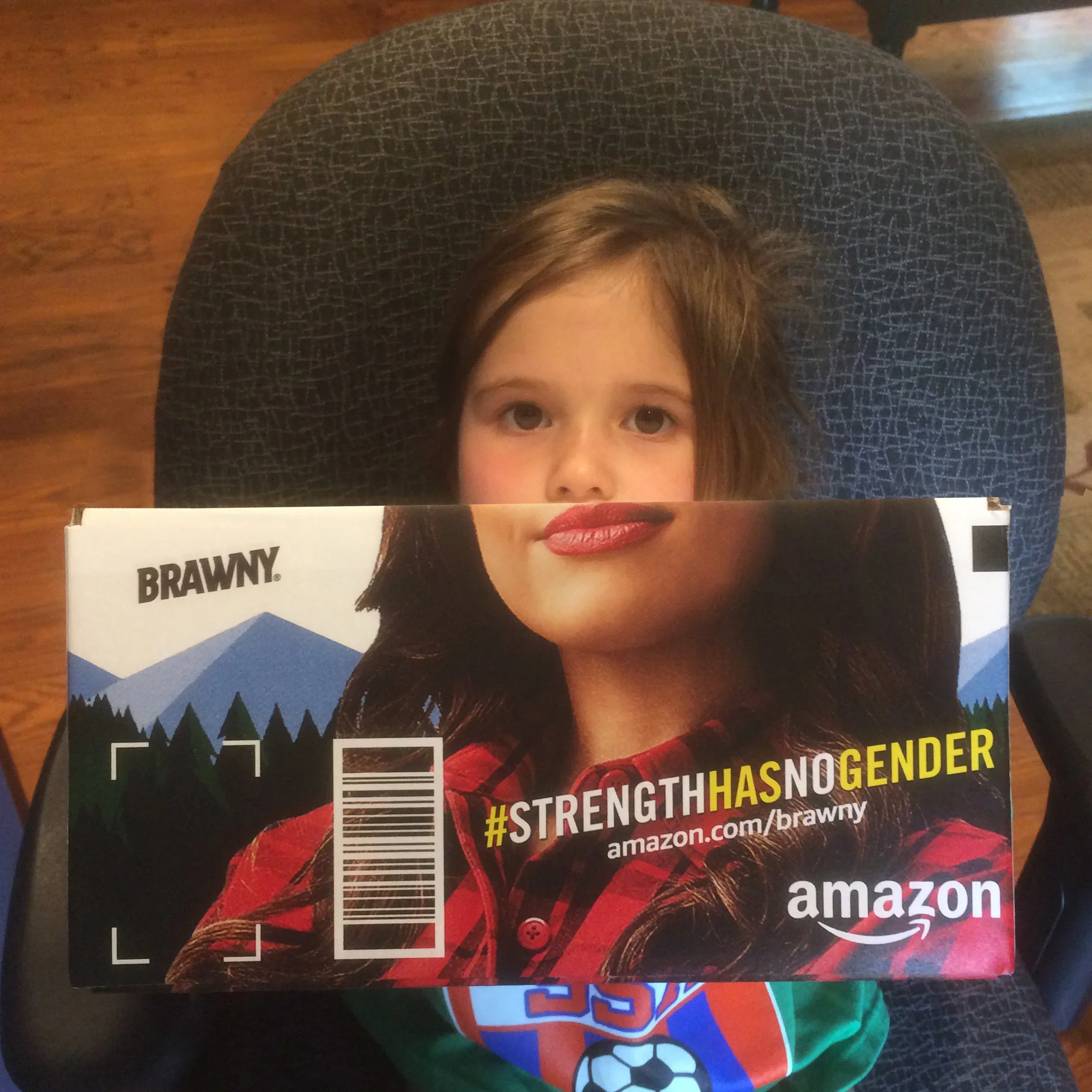 Close-up of a magazine cover featuring a child's face, with an emphasis on the child's eyes and nose. The page is partially covered by a coloring book or another magazine with a sports theme, showing a soccer ball and a person wearing a red and black plaid shirt. The text includes hashtags and website links related to Amazon.