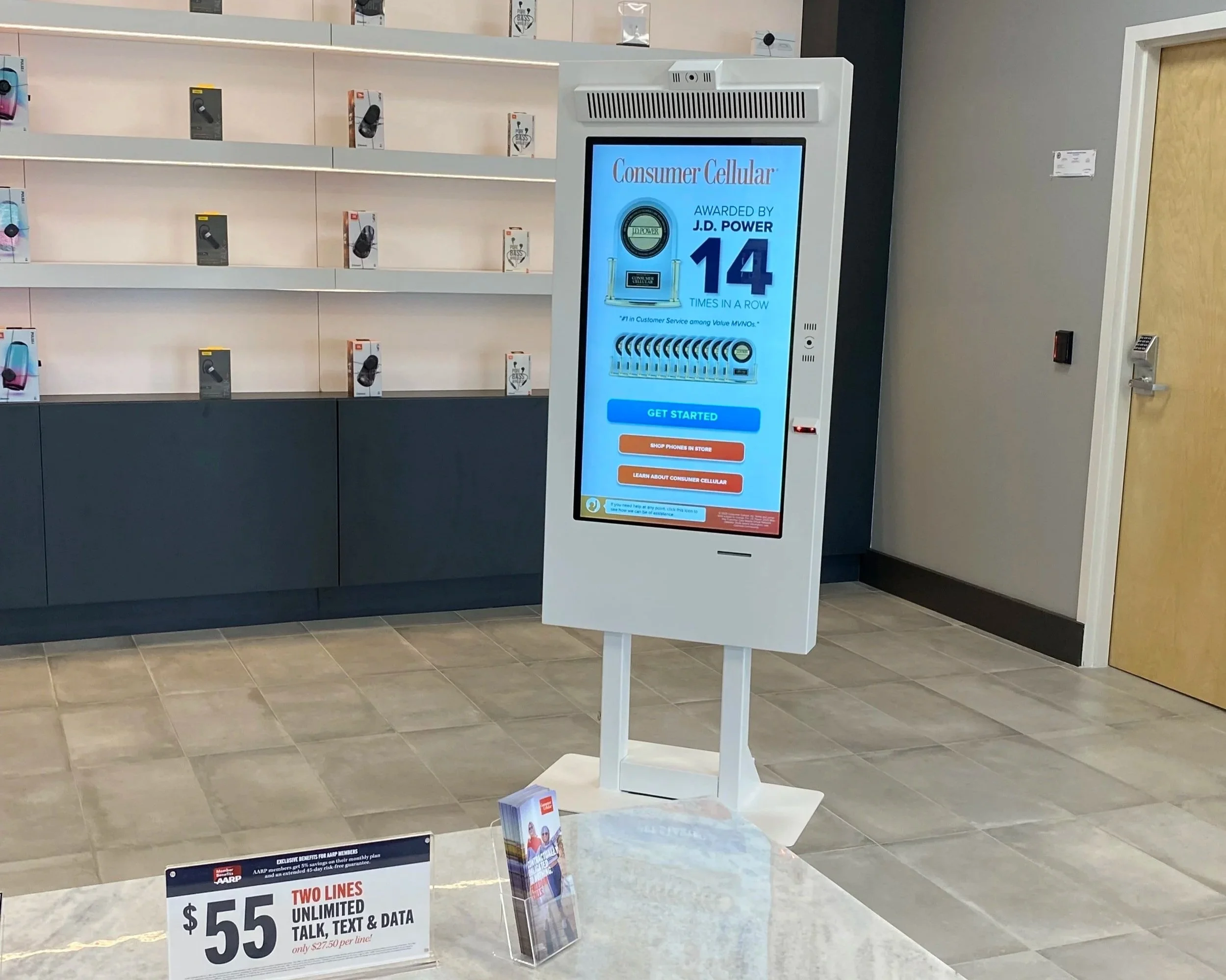 A digital display advertising wireless phone plans in a store with empty shelves and a door nearby.