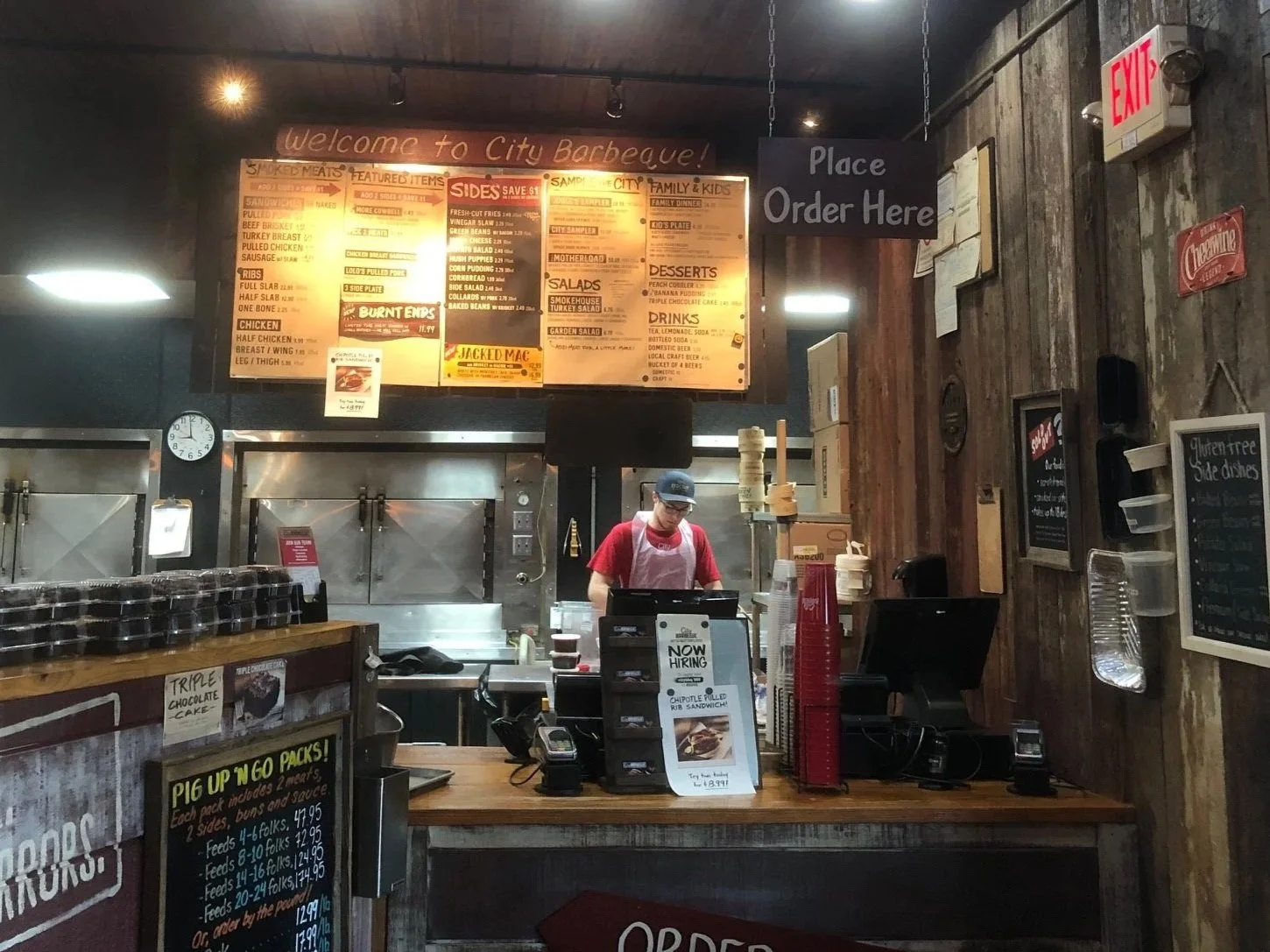 Interior of a barbecue restaurant with a worker at the counter, menus hanging on the wall, and a sign that says "Place Order Here."