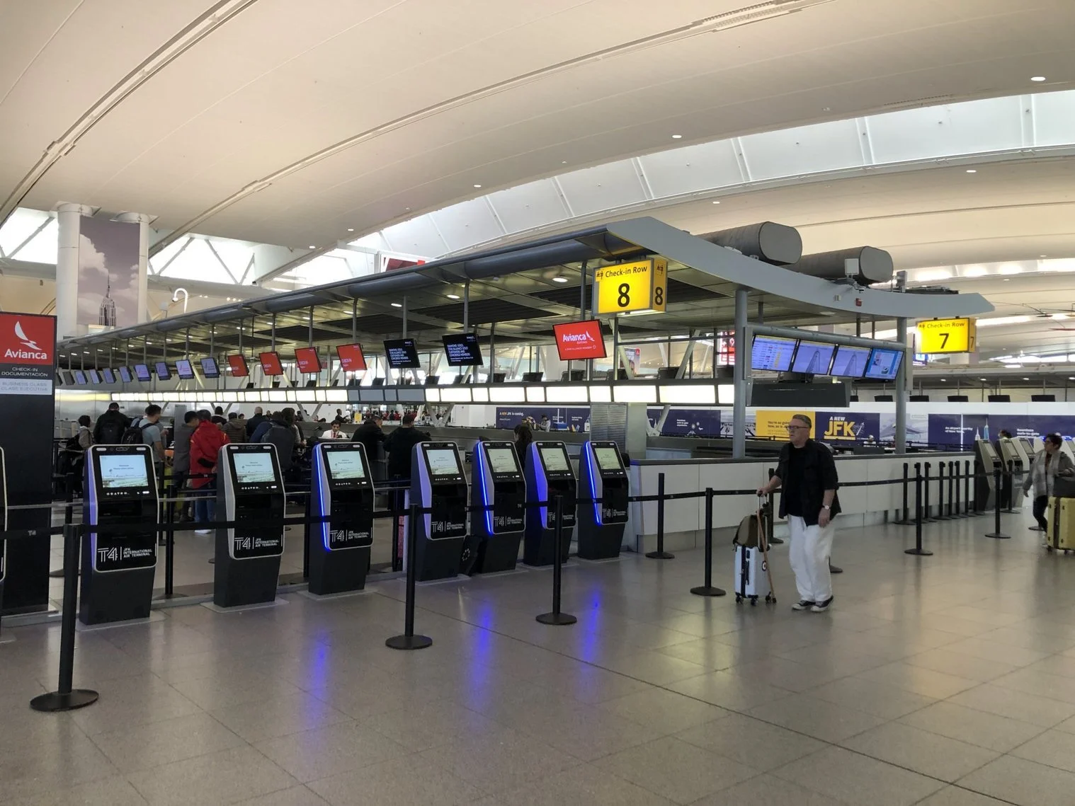 Airport check-in counter with digital screens and kiosks, travelers with luggage, and signage for rows 7 and 8.