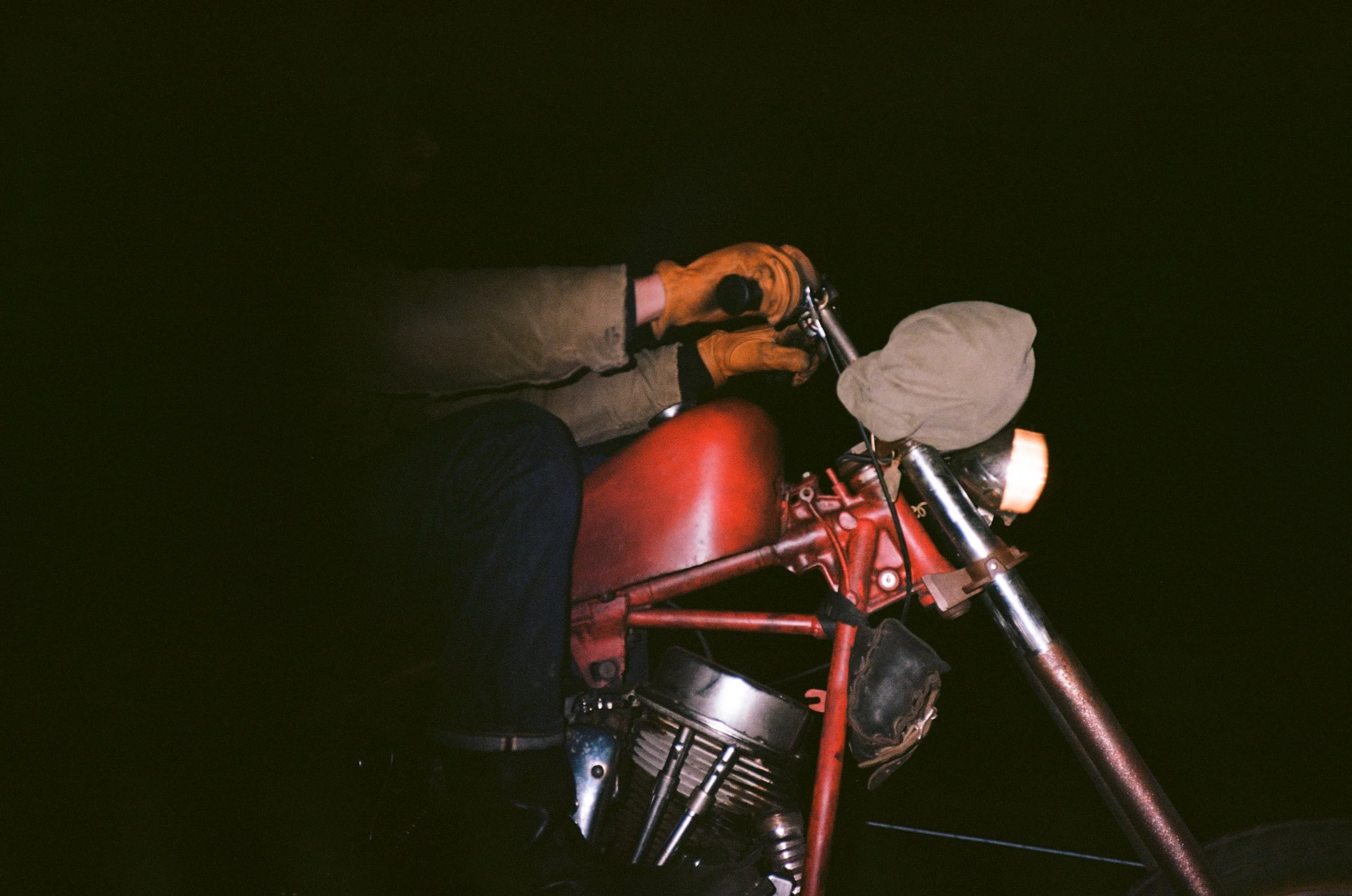 A person wearing yellow gloves riding a red motorcycle at night.