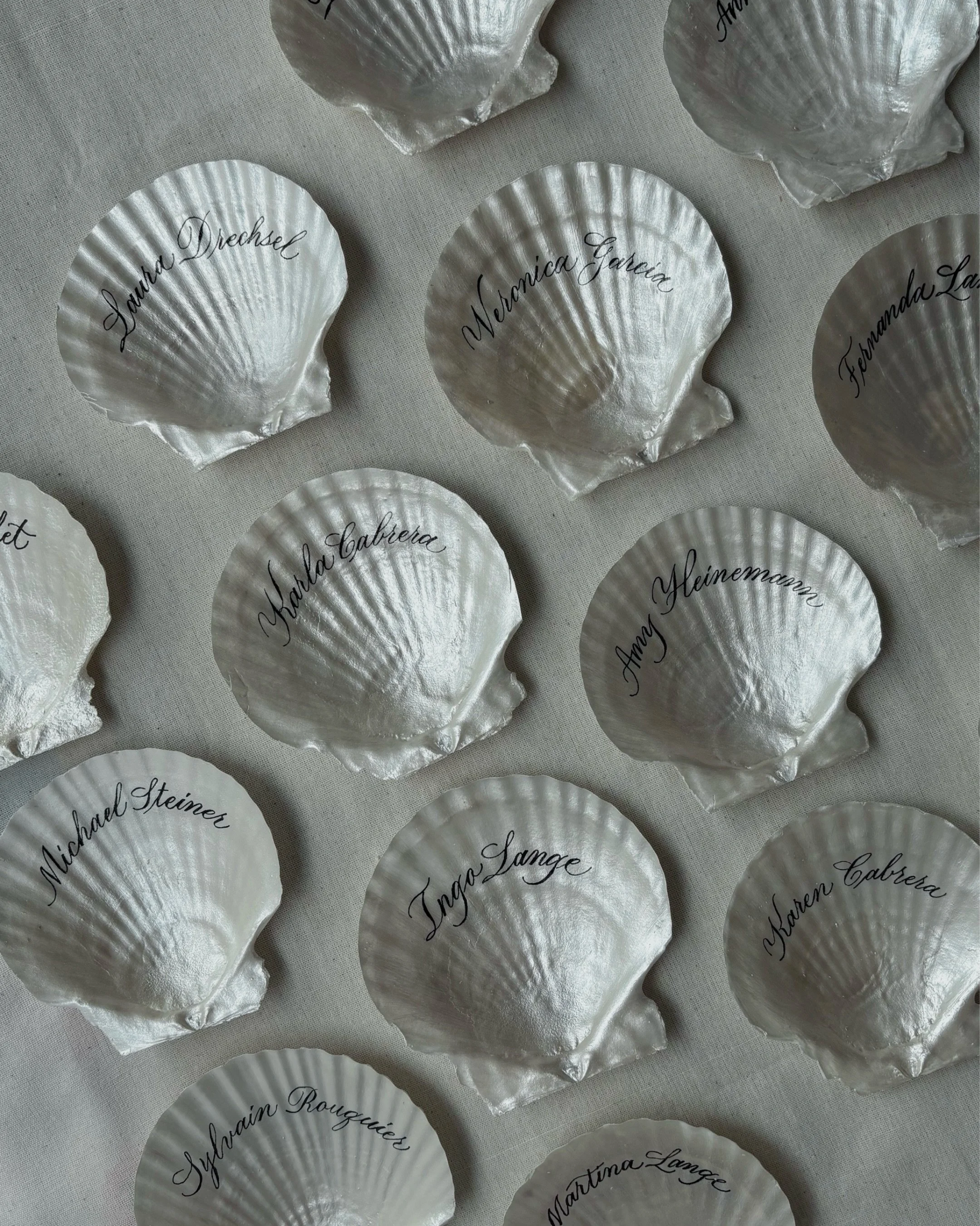 A place for every name, and a little keepsake to take home.

These real seashells were hand-painted in a soft pearlescent finish, then carefully calligraphed one by one with each guest&rsquo;s name. A final coat of varnish adds a glossy finish while 