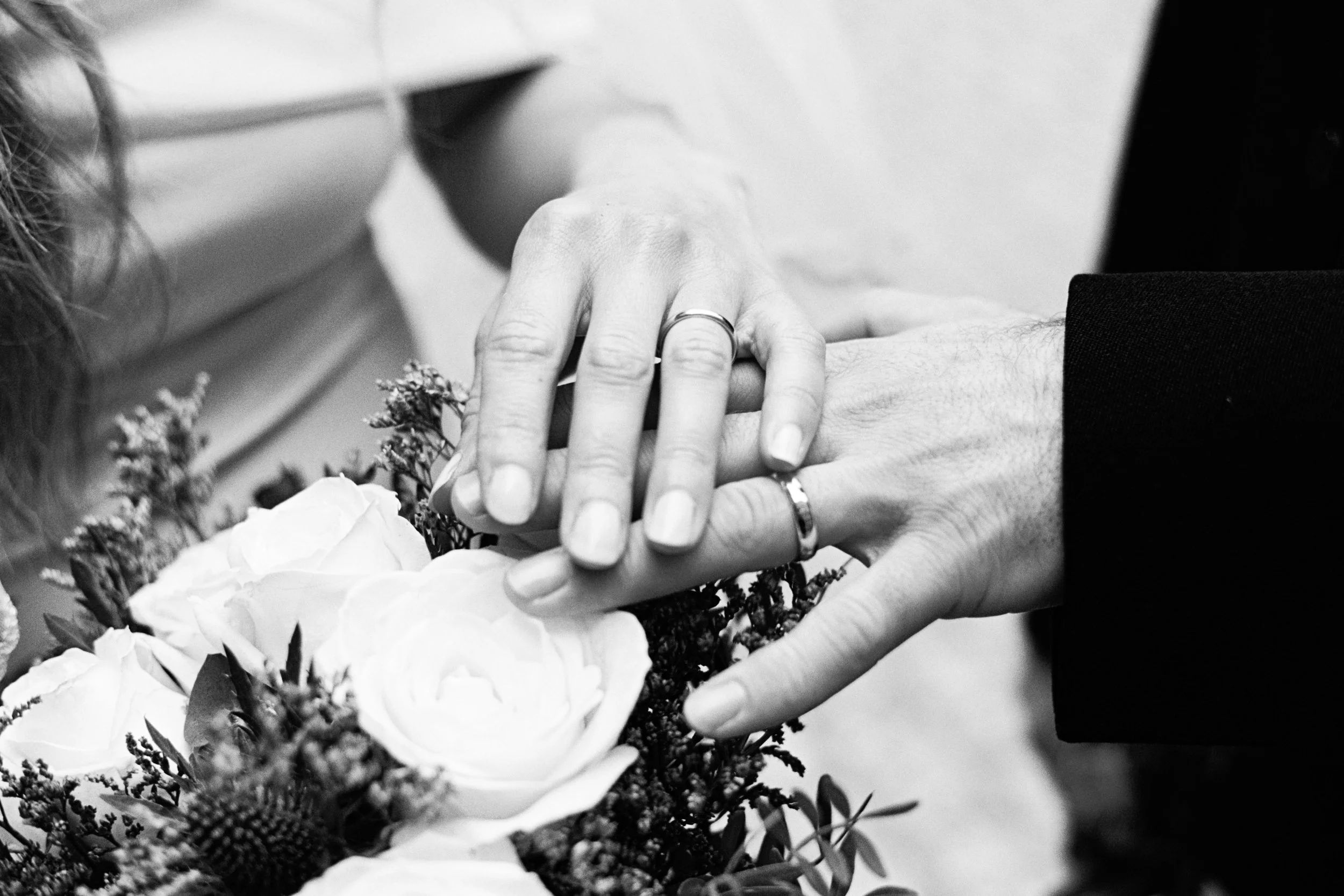 Close-up of a person holding a bouquet of flowers, showing their hand with wedding rings, possibly at a wedding or special event.