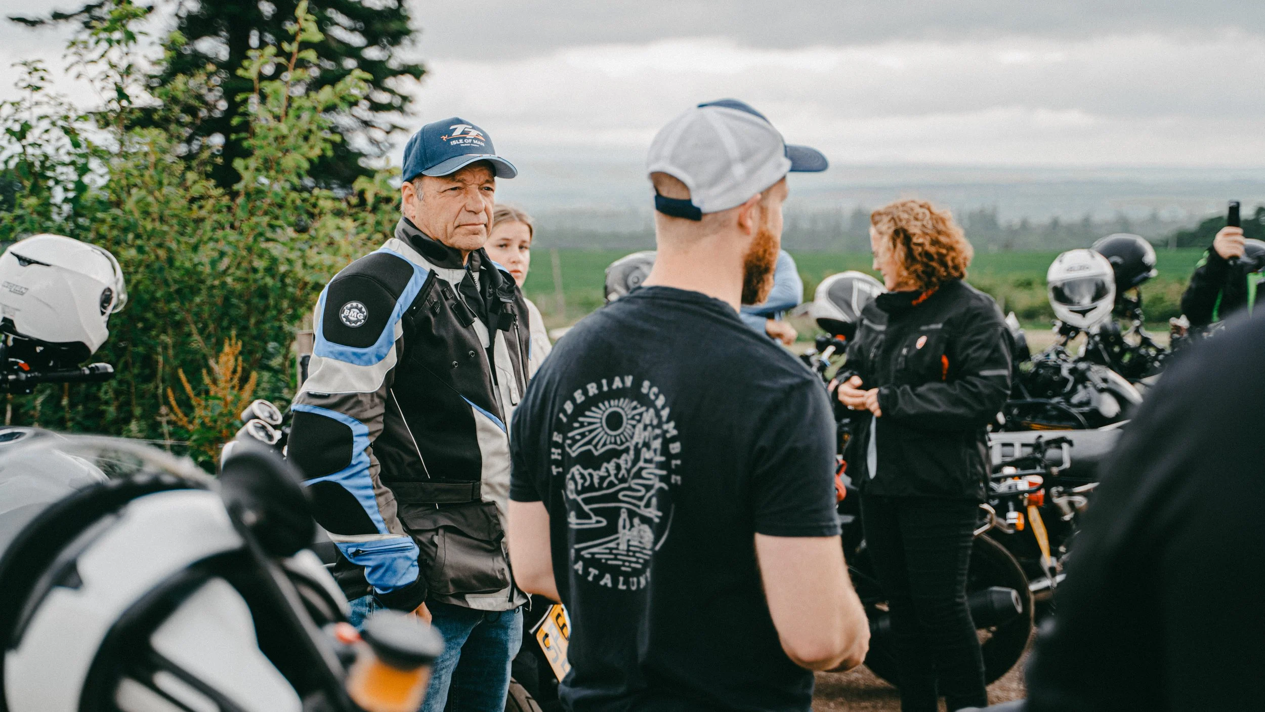 Group of motorcyclists gathered outdoors near motorcycles during cloudy weather.