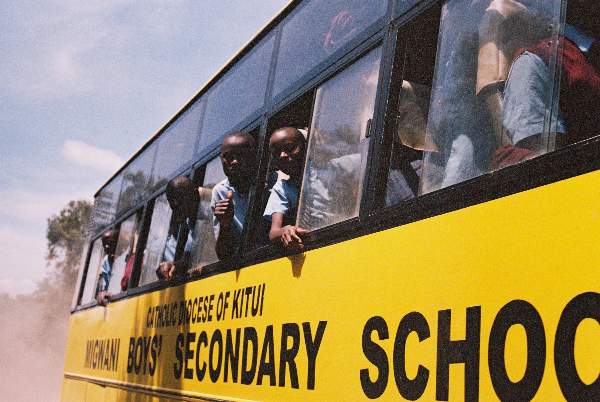 Children looking out from the windows of a yellow bus.