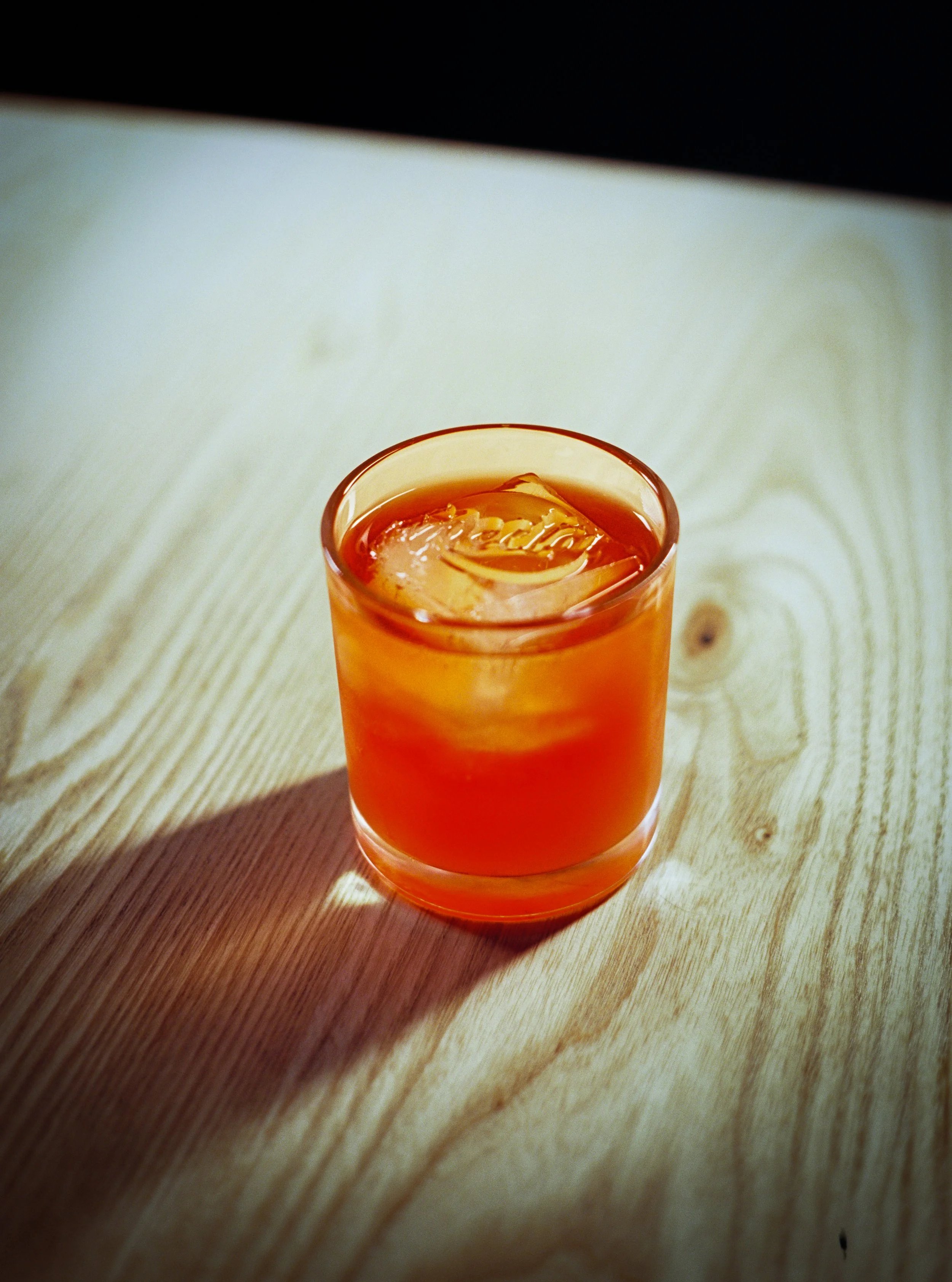 Close-up of a glass with amber-colored beverage and ice cubes on a wooden surface.