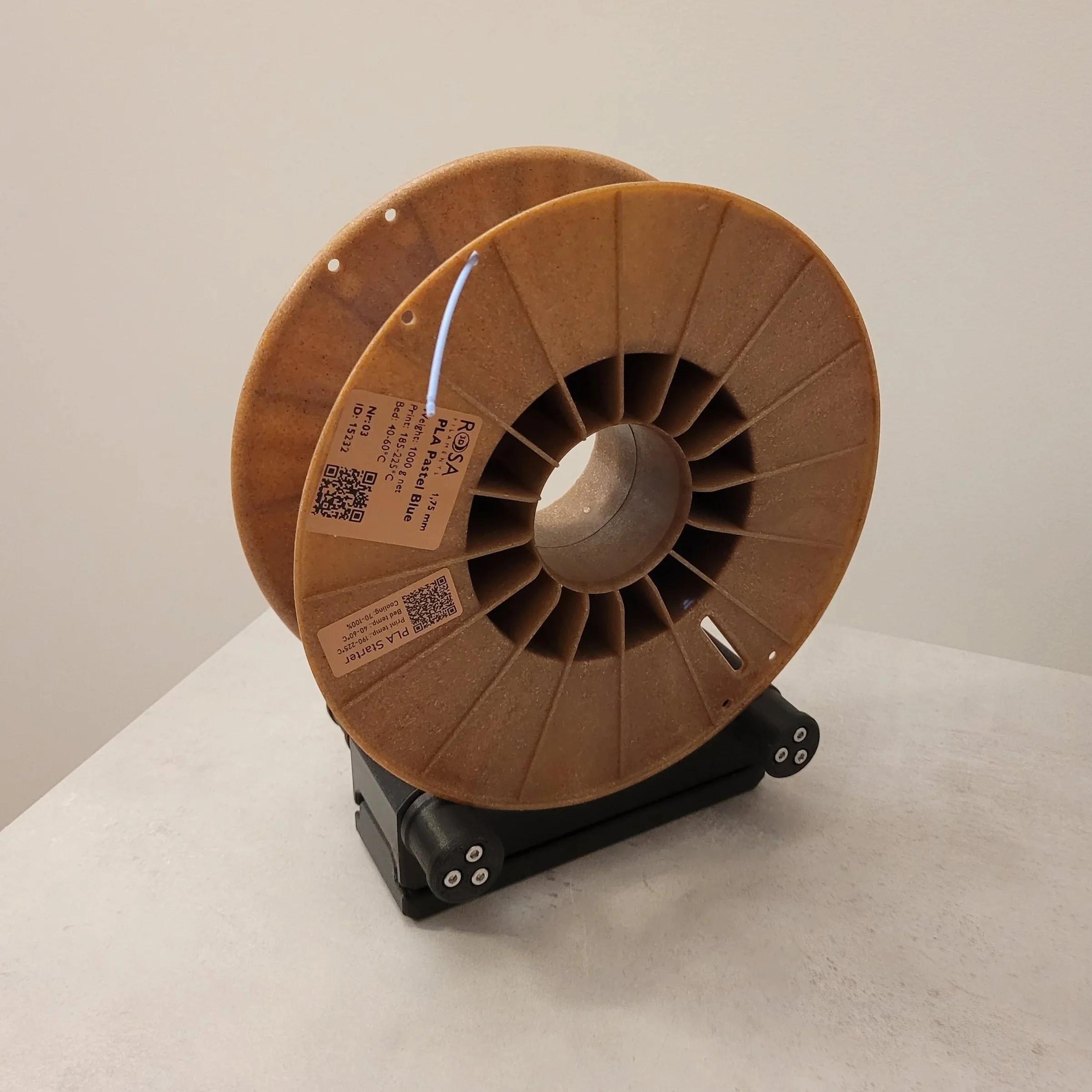 Close-up of a brown cardboard spool with a white string, placed on a black base, against a plain light-colored background.