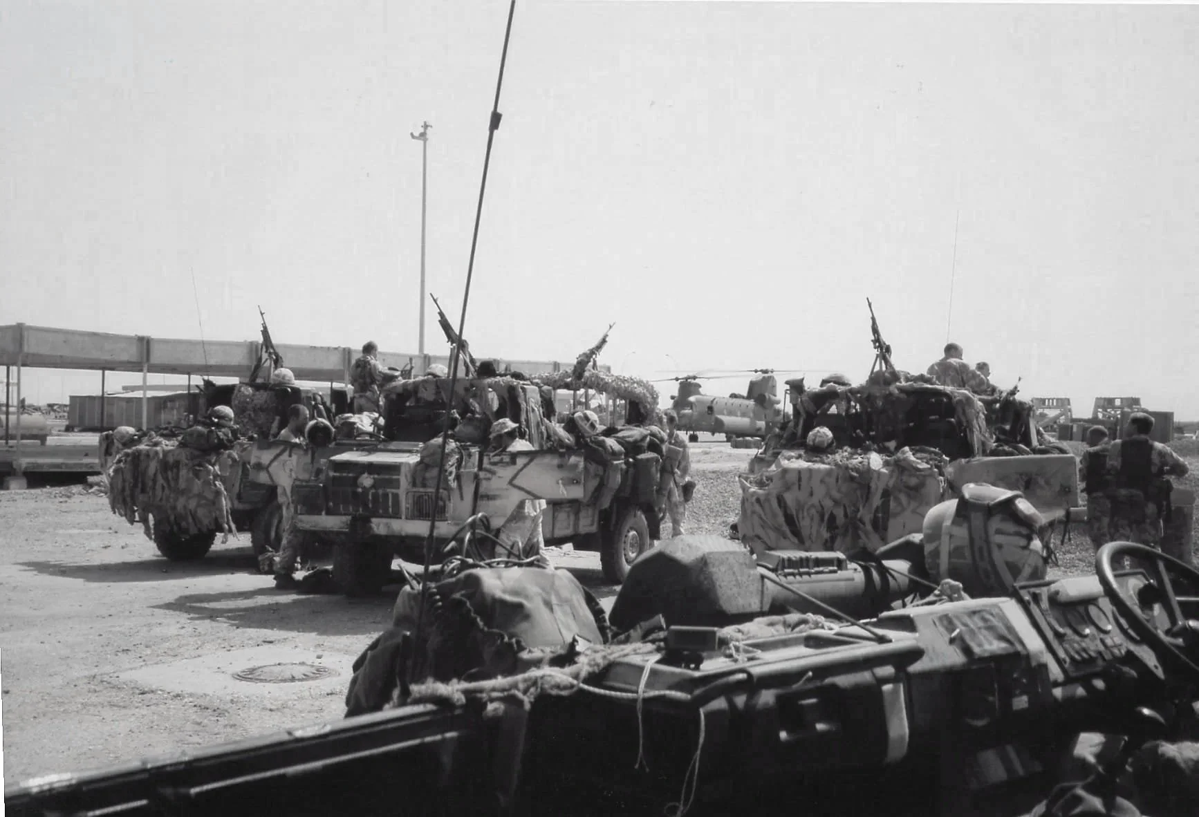 Black and white photo of military personnel and vehicles with some equipment and supplies, possibly at an airstrip or military base.