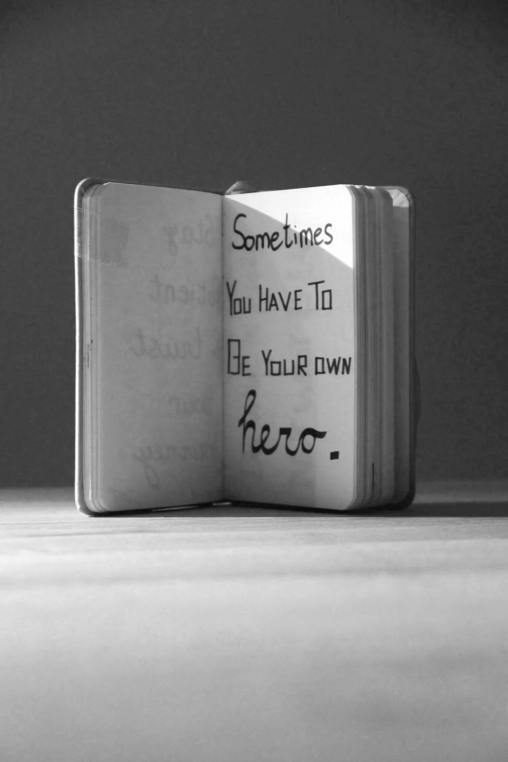 Open notebook on a flat surface with handwritten text reading, 'Sometimes You Have To Be Your Own Hero'.