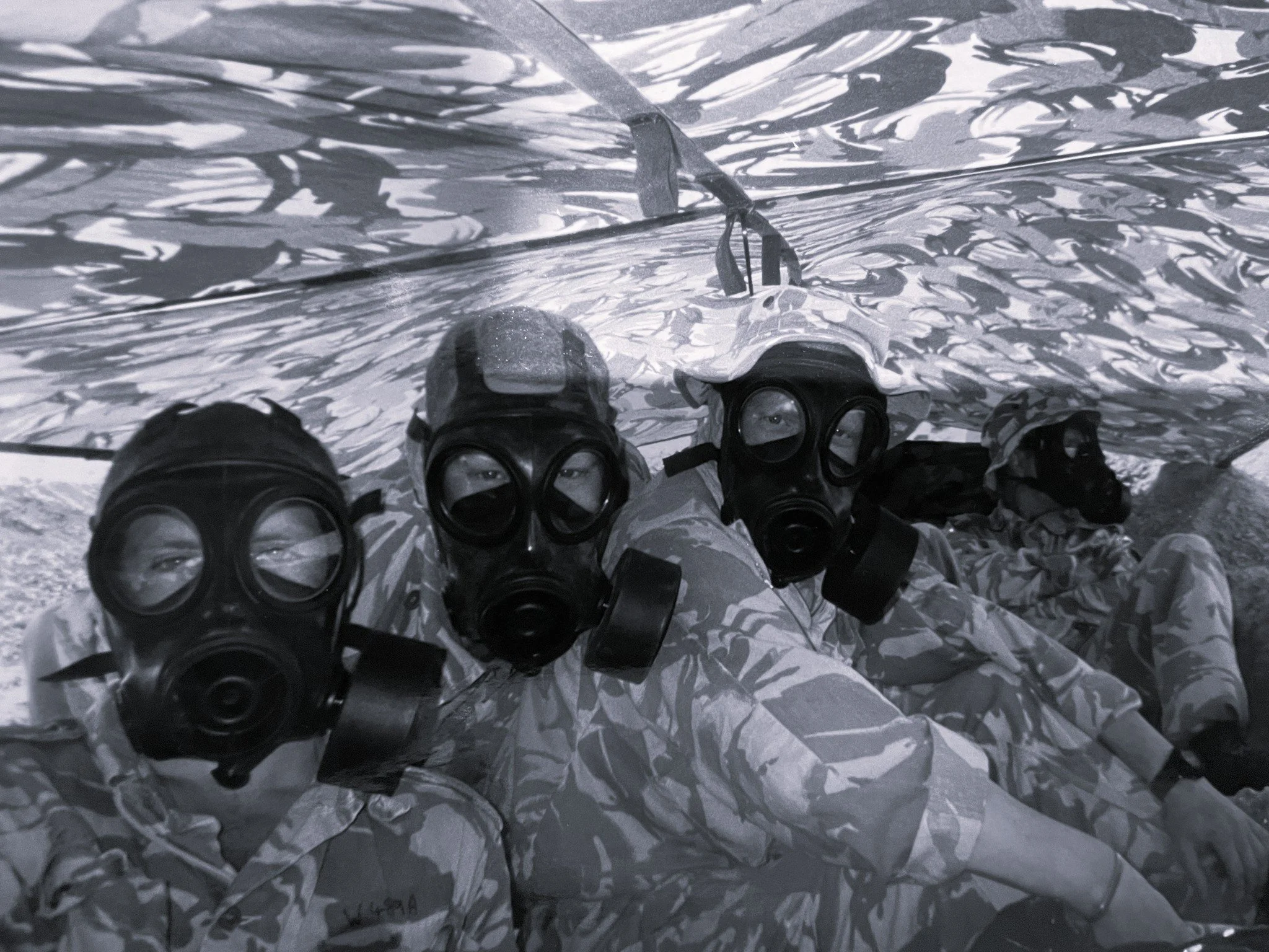 A person wearing a wetsuit, goggles, and a snorkel holds a transparent plastic bag filled with water and rocks, standing in front of a textured crinkled metallic surface.
