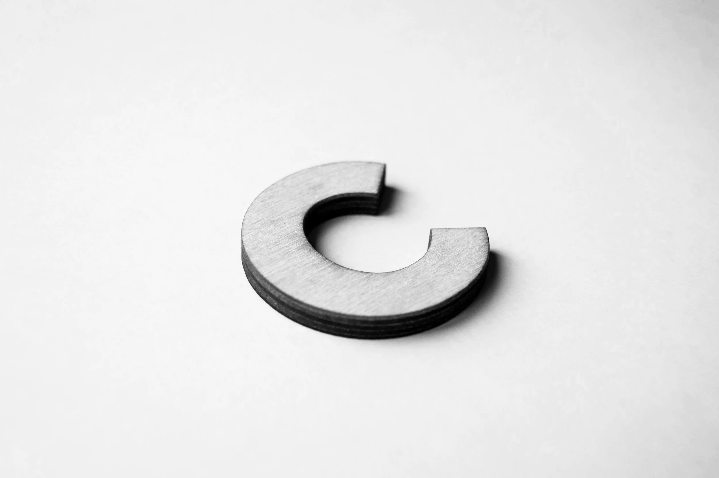 A metallic letter 'C' resting on a white surface.