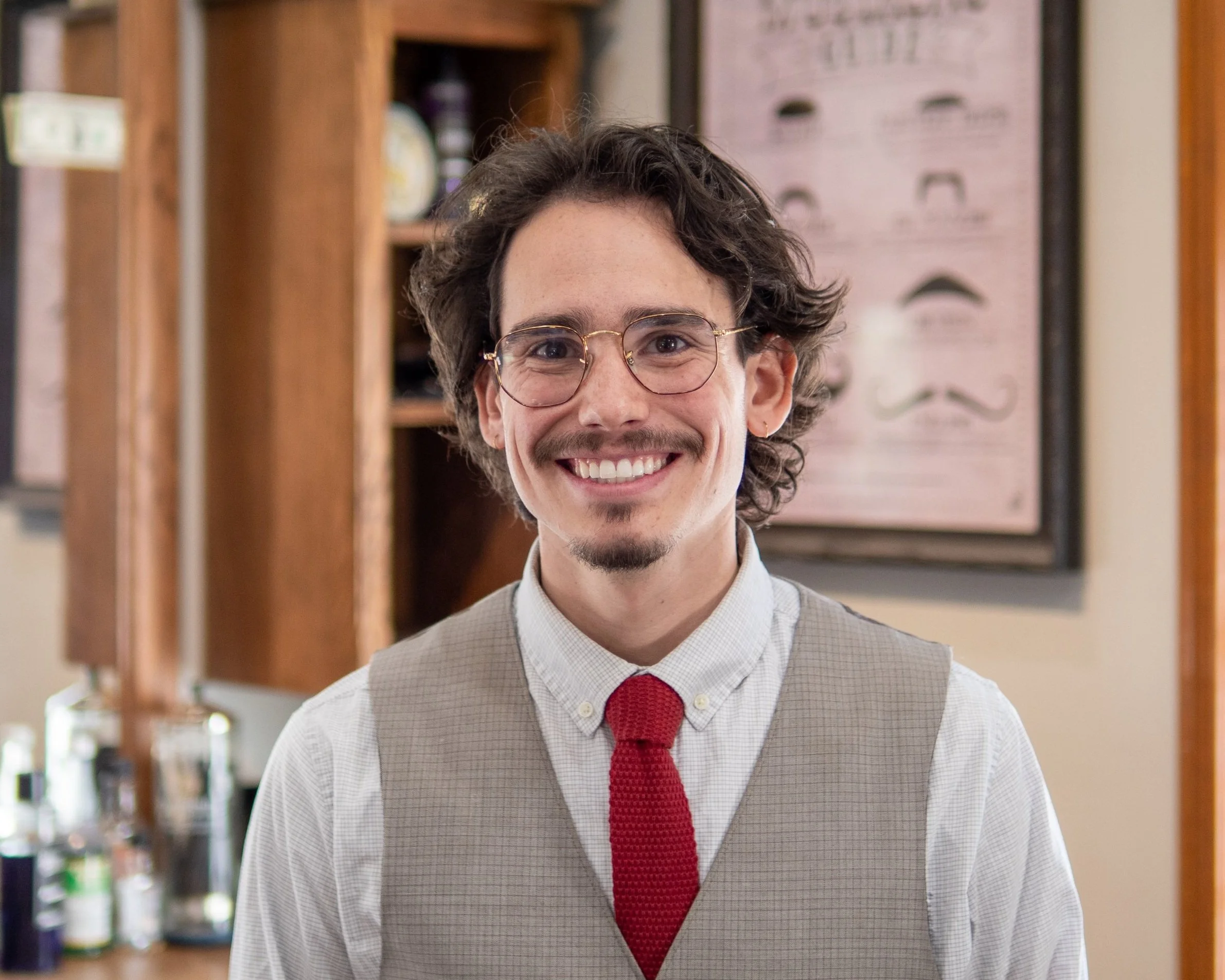Man with glasses and a red tie smiling in a barbershop setting.