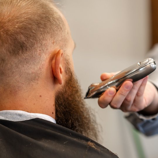 Barber using clippers to trim a man's beard in a barber shop.