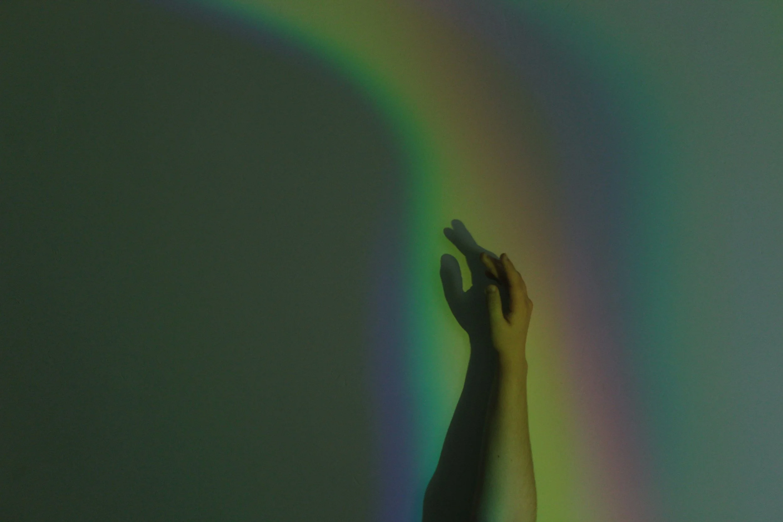 A hand reaching toward a rainbow-colored light projection on a wall.