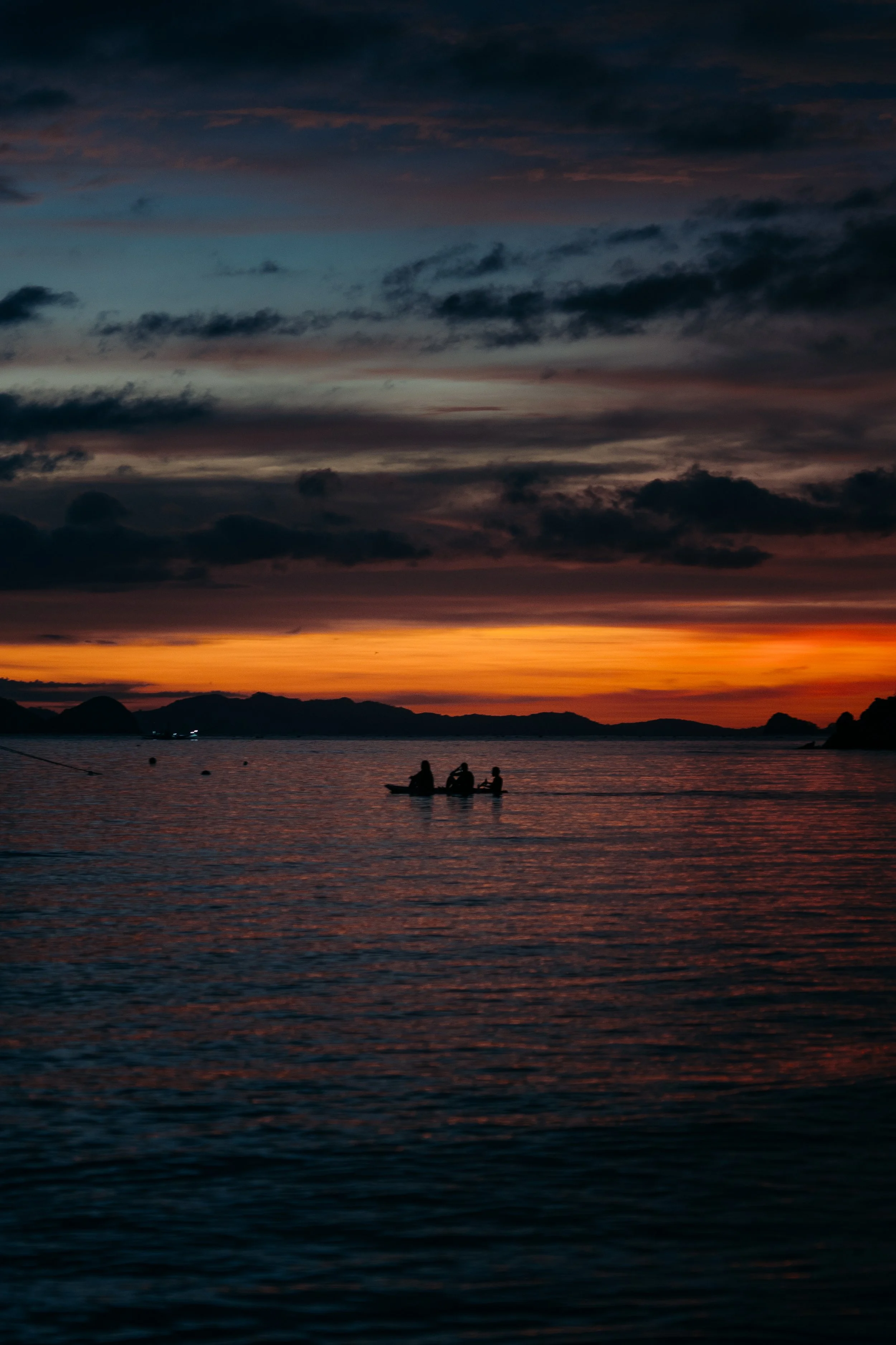 atardecer sobre el mar con nubes oscuras y tres personas en bote en el agua.
