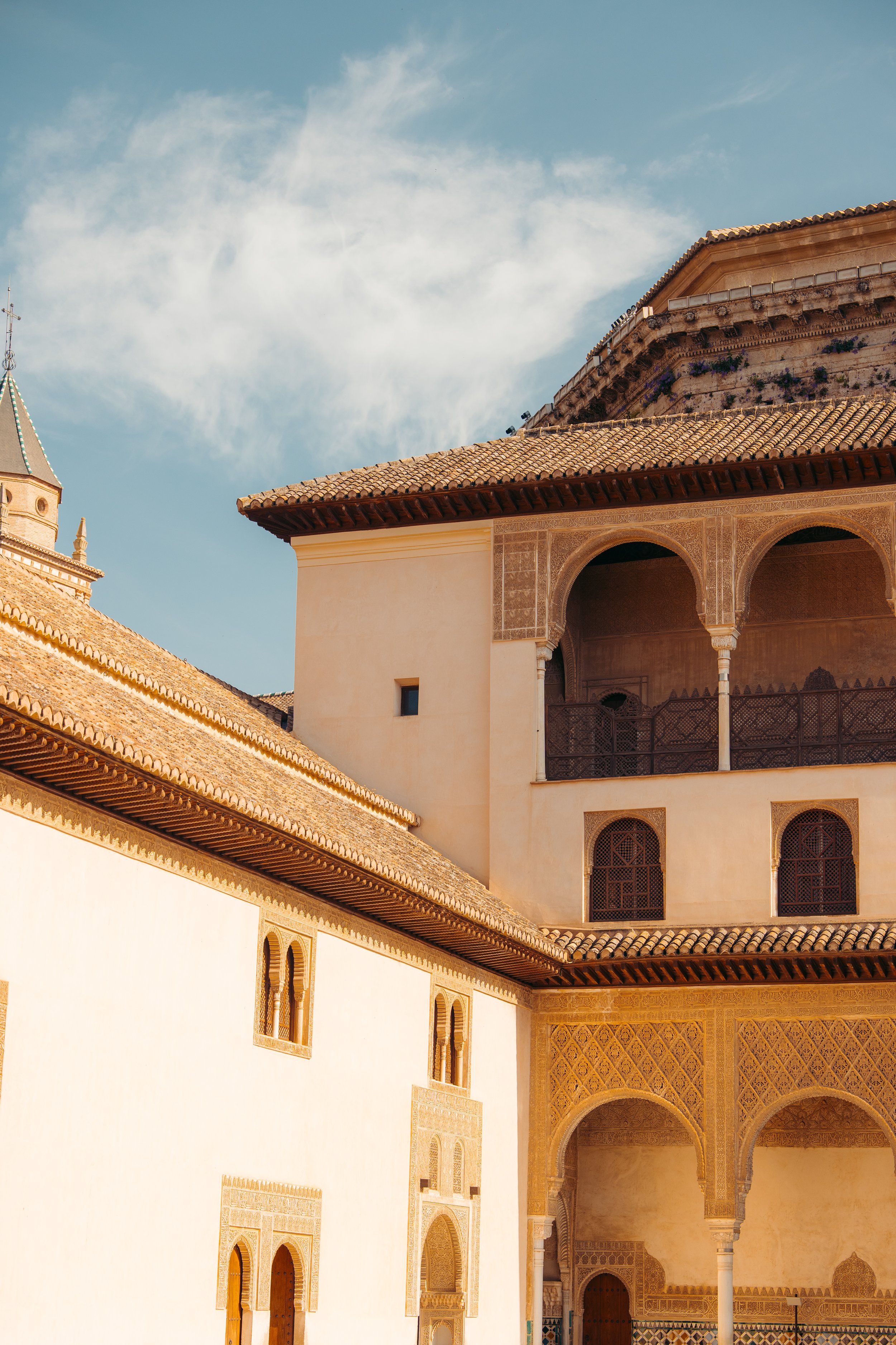 Imagen de un edificio con arquitectura tradicional andalusí, con paredes blancas, ventanas con enmarcado de intrincados diseños y techos de tejas rojas, bajo un cielo azul con algunas nubes.