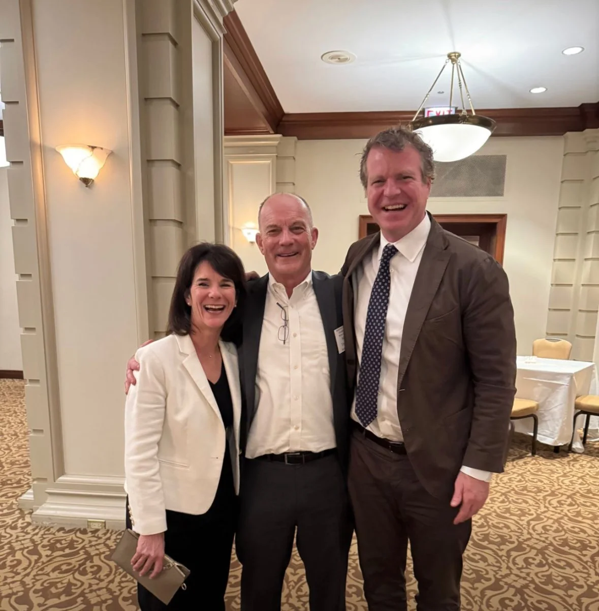 Three people, two men and one woman, smiling and posing together in an indoor setting with warm lighting and beige walls. Dr. Jennifer Posa with colleagues 