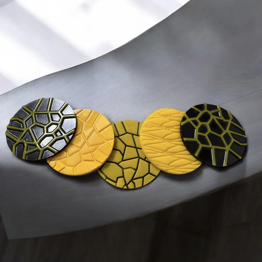 Five decorative round objects with geometric patterns in black, yellow, and green, arranged in a row.