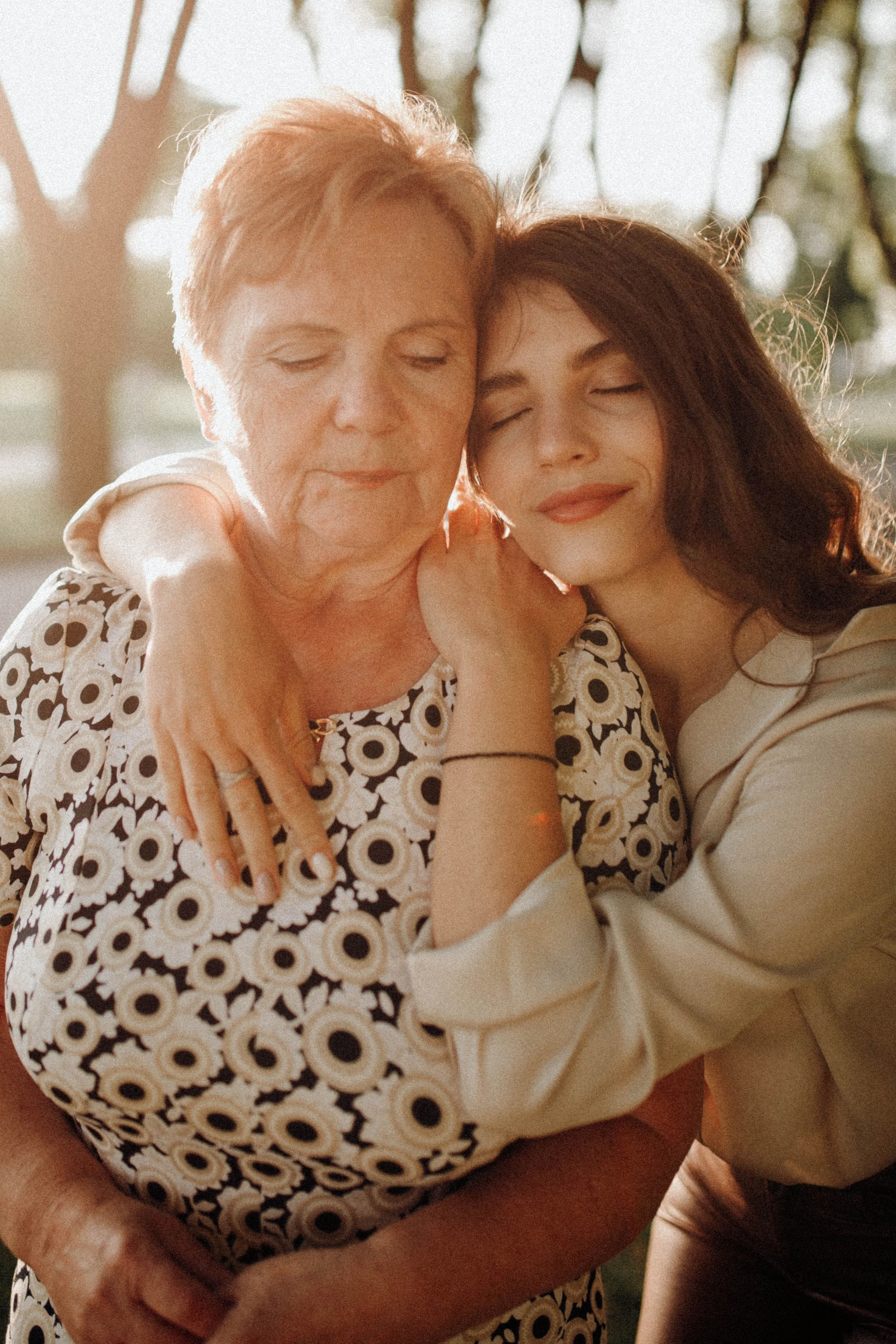 An older woman embracing her adult daughter warmly outdoors, representing the close family bond at the heart of senior living decisions.