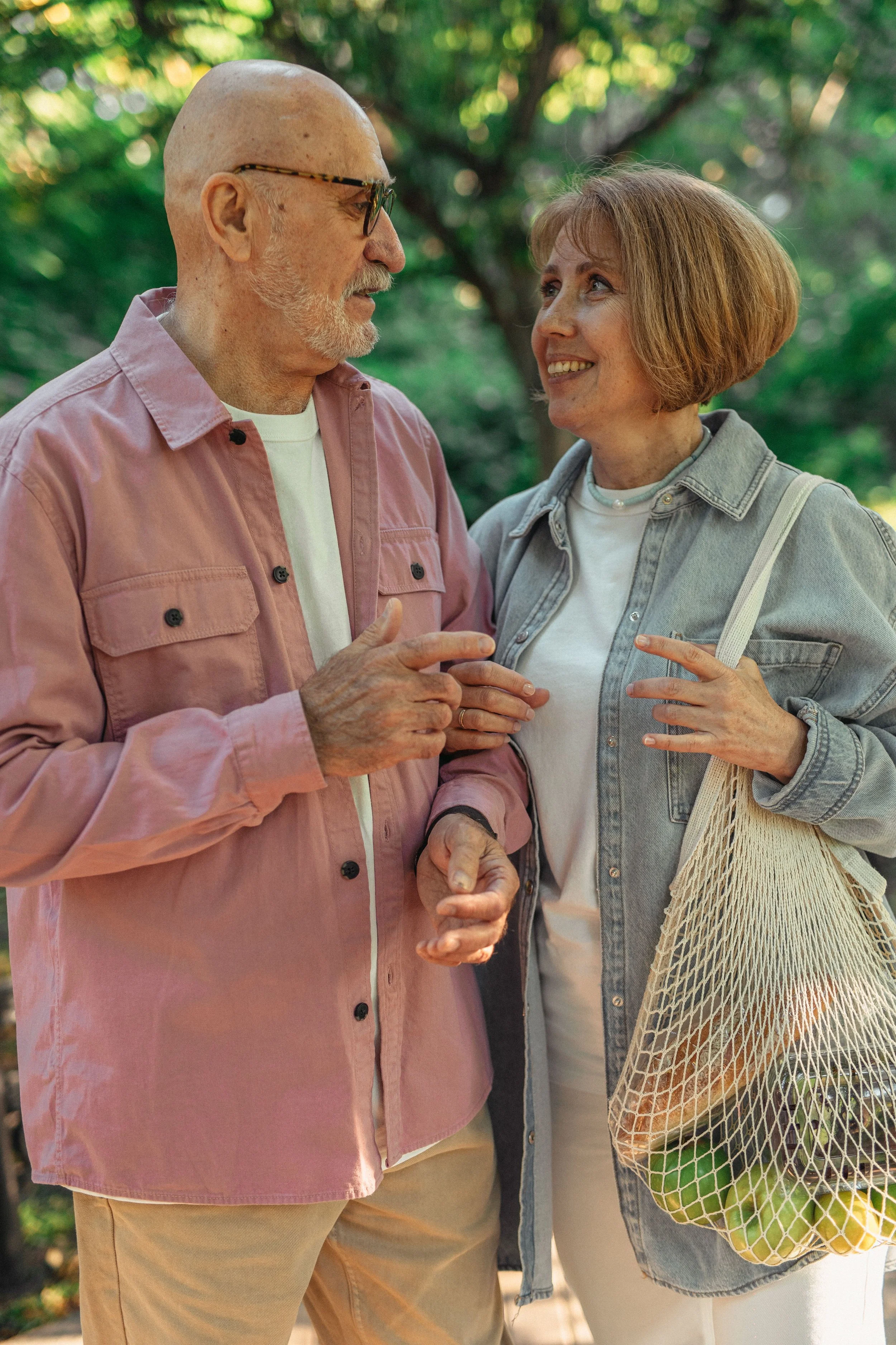 An older couple smiling and talking warmly outdoors while carrying groceries, representing a happy stage of senior life.