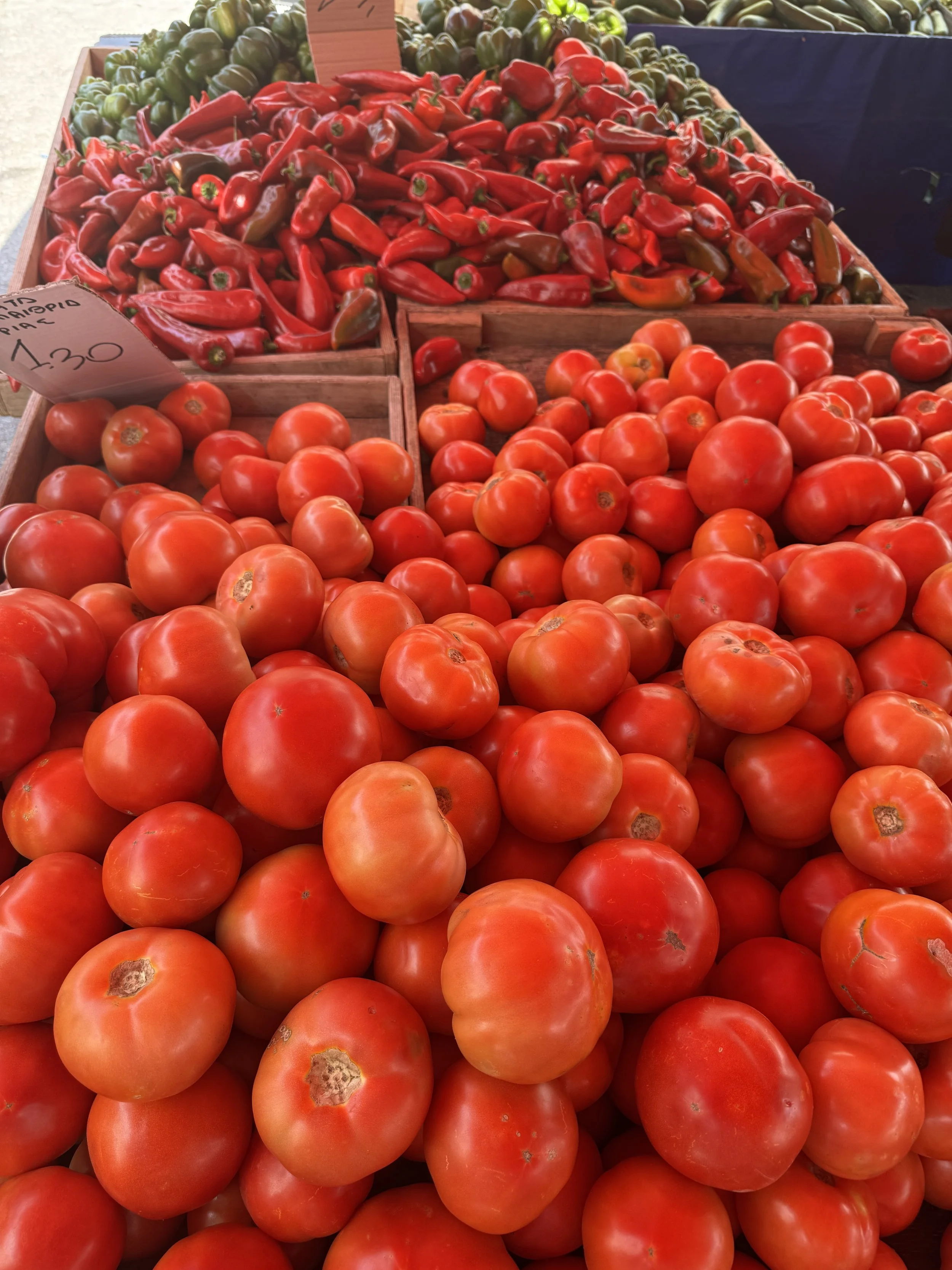 Fresh tomatoes and red peppers displayed in wooden bins at a farmers market