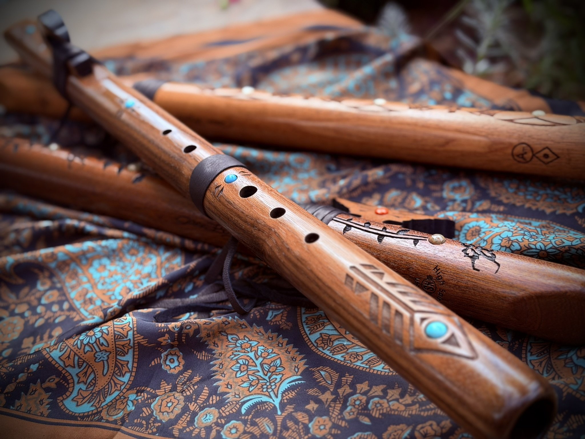 Close-up of two wooden flutes with carved designs, resting on a patterned fabric with floral and geometric motifs in shades of blue, orange, and black.