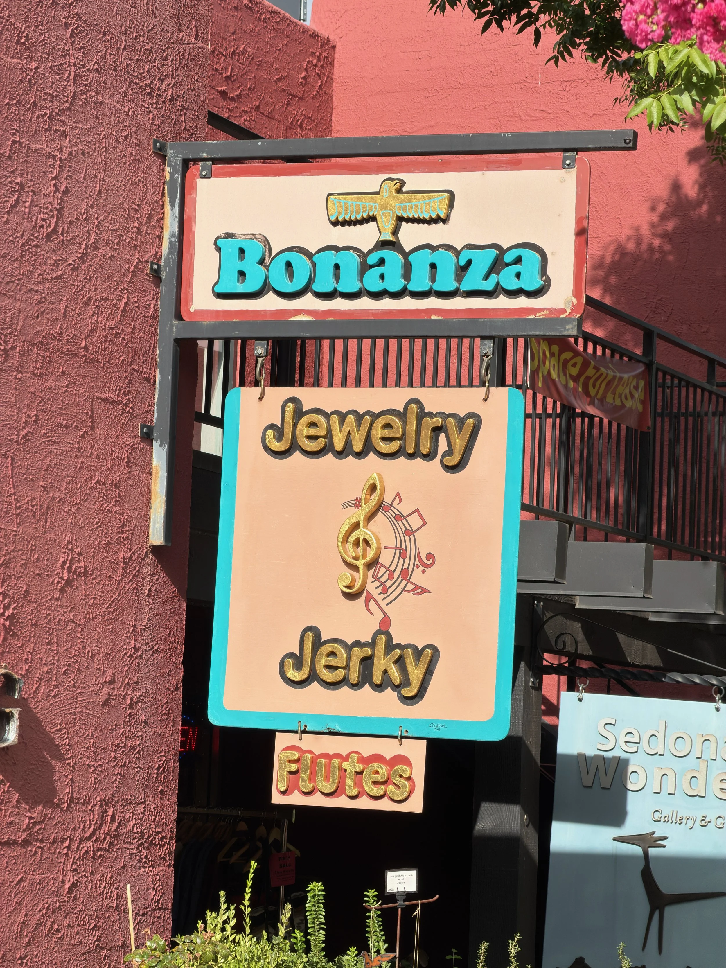 Storefront sign displaying the name 'Bonanza' with a turquoise font, a golden eagle symbol above, and a smaller sign below reading 'jewelry' in gold letters. Additional signage for 'flutes' and other shops is partially visible.