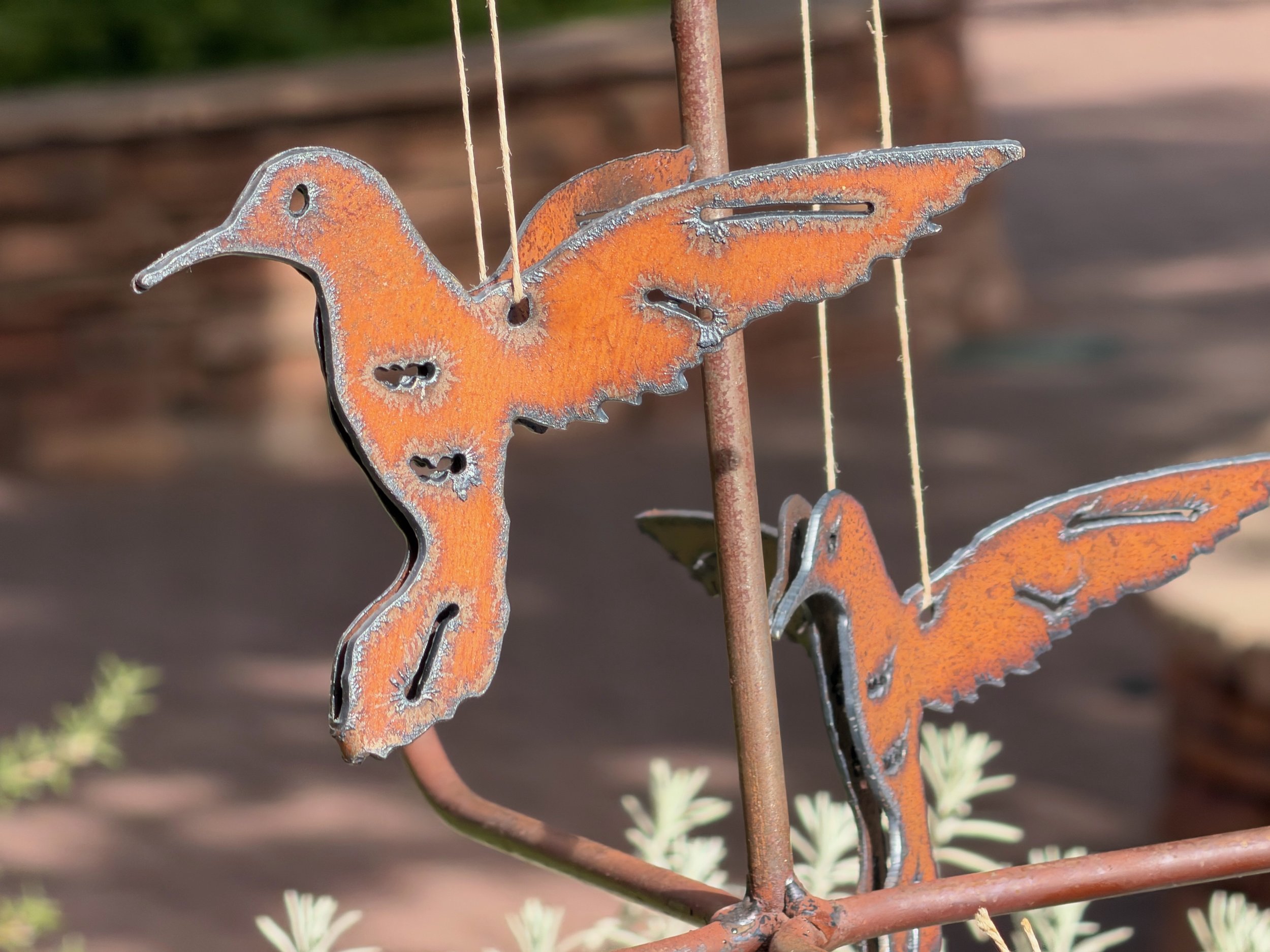 Close-up of a rusted metal butterfly garden decoration with orange coloring and cut-out details, mounted on a vertical metal stake in a garden setting.