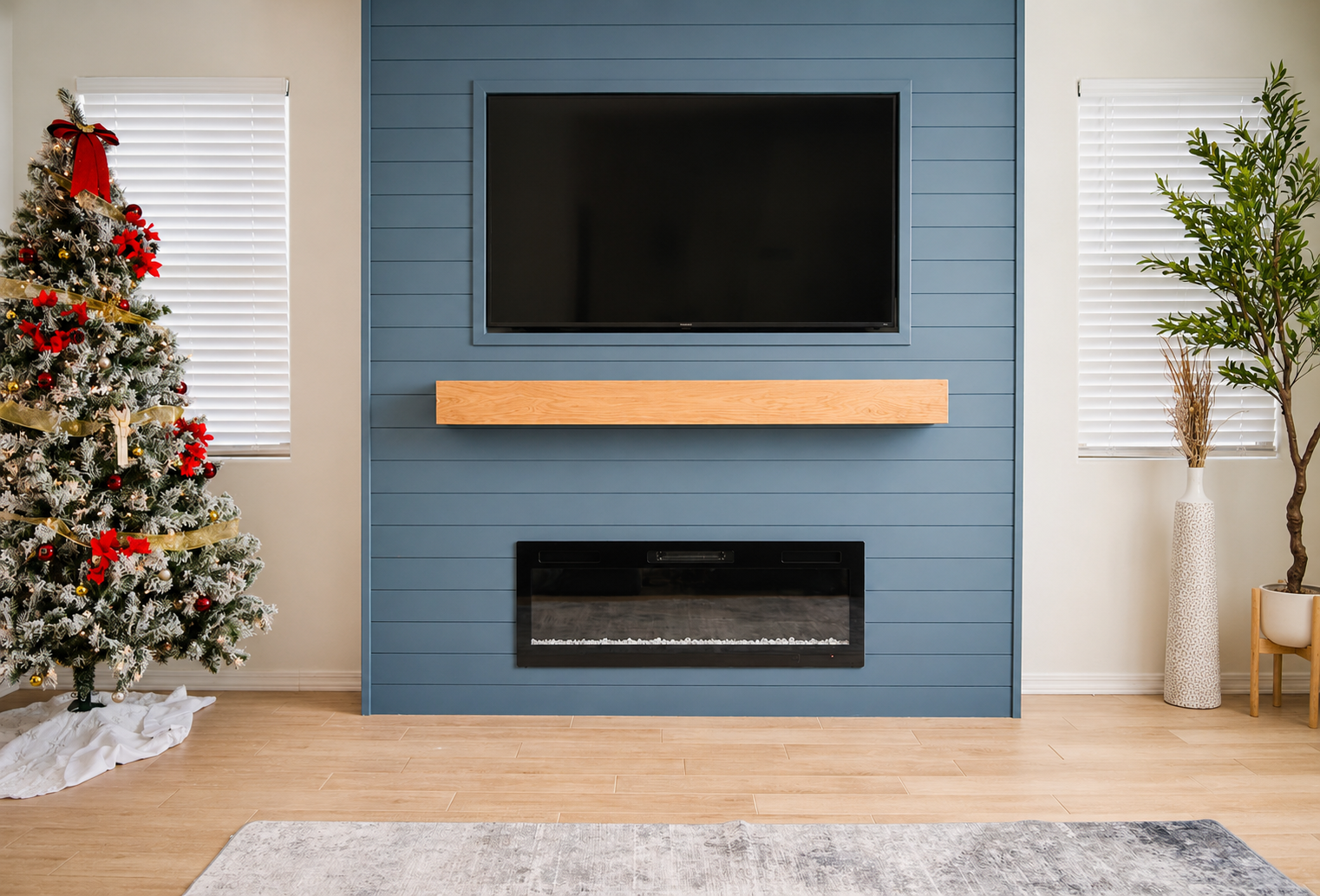 Living room with a Christmas tree decorated with red bows, ribbon, and ornaments on the left, a blue accent wall with a mounted television, an electric fireplace, and a plant in a white pot on the right.