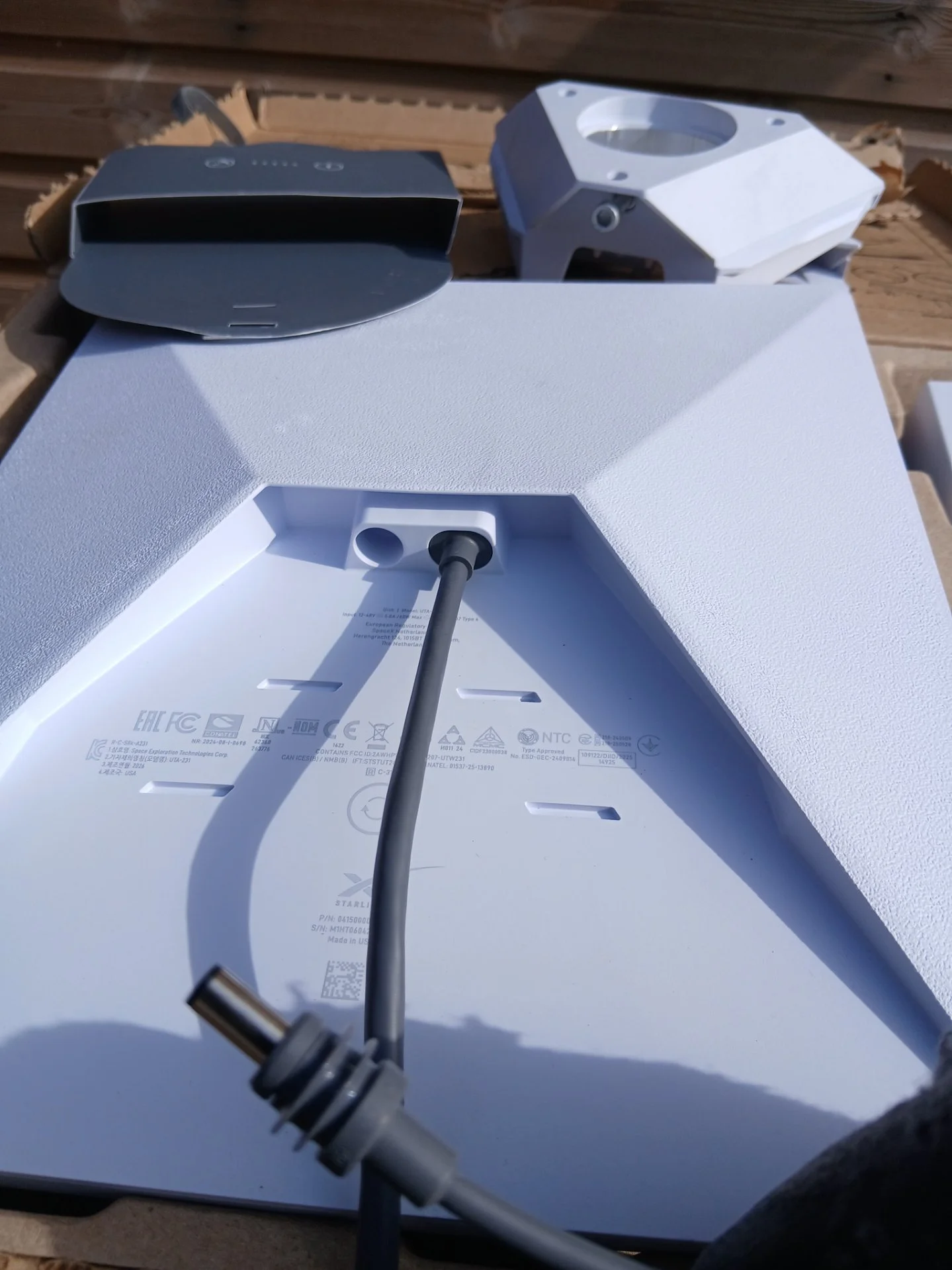 Back of a Starlink mini dish with a black power cord inserted into it, laying on a protective surface before installation