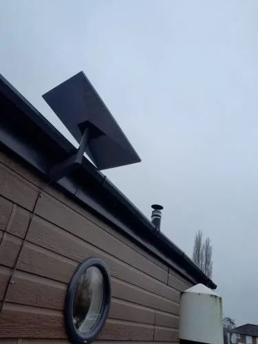 A satellite dish mounted on the side of a building under an overcast sky.