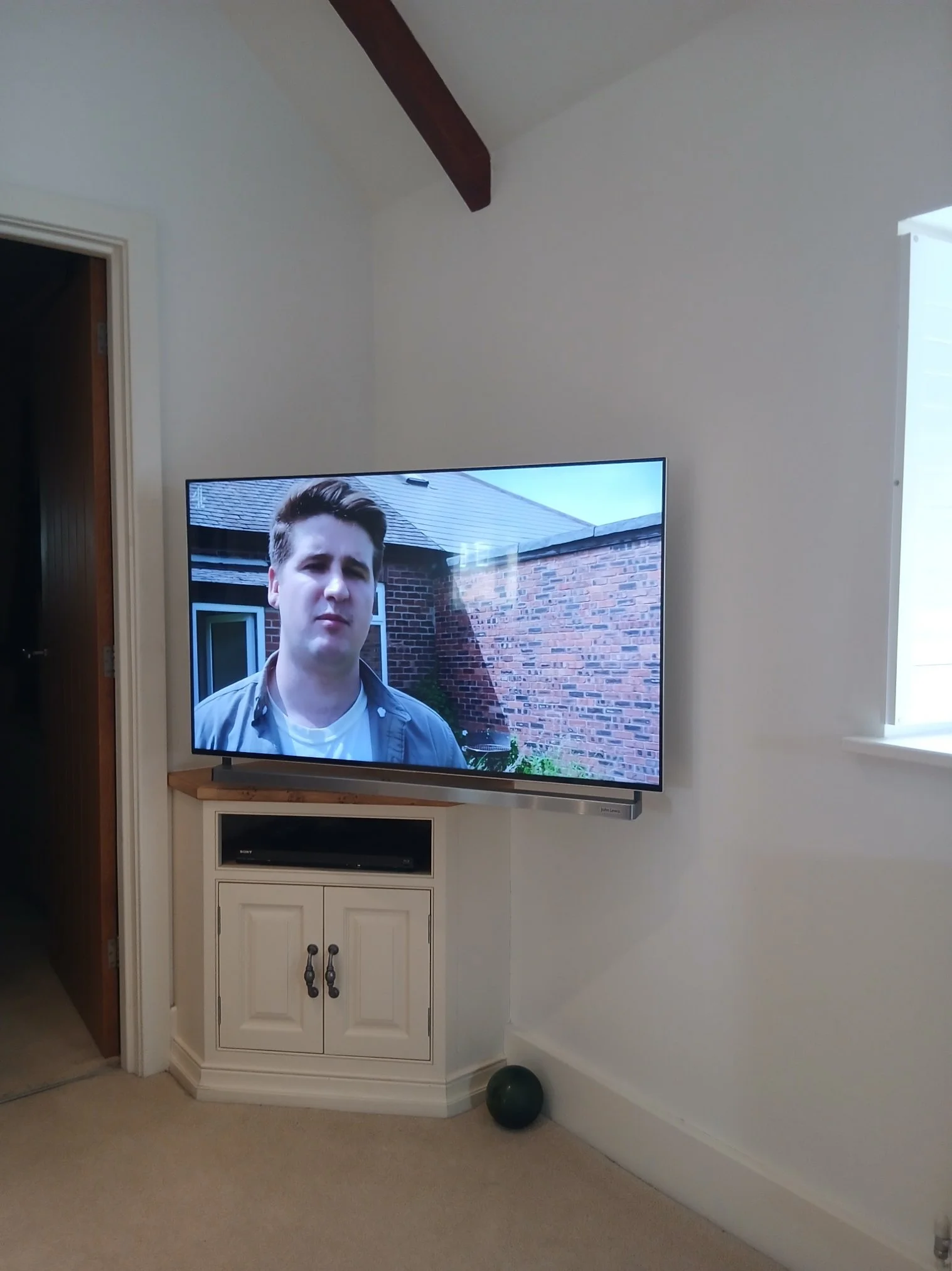 Living room corner with a multi position wall bracket mounted to a flat-screen TV showing a young man outdoors.