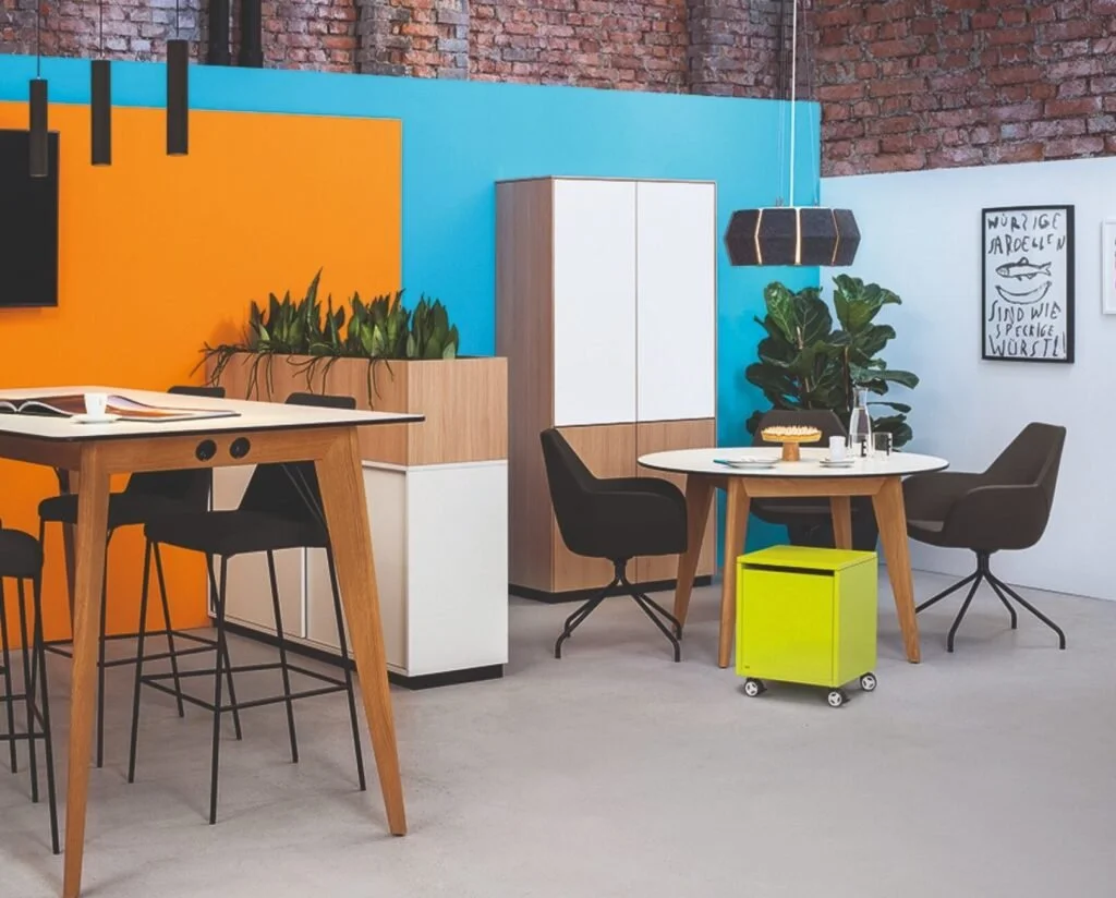 Modernes Büro mit bunten Wänden, Esstisch, Stühlen, Grünpflanzen, Wanddeko und einer Stehlampe, eingerichtet von hali Büromöbel. smarte, variantenreich und bunte Büromöbeleinrichtung. Fun at work.