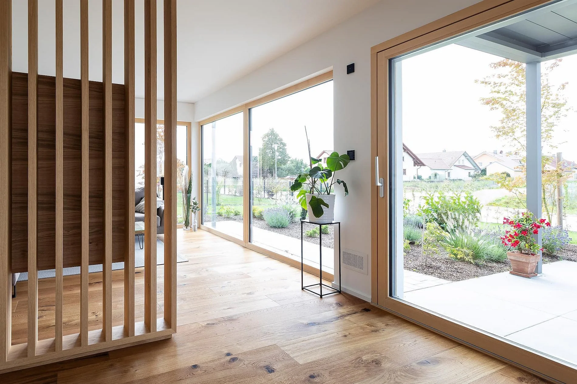Innenansicht eines Hauses mit großen Fenstern und Terrassentür von Gaulhofer , Holzboden, Pflanzen und Garten im Hintergrund. Holzfenster-Pionier.