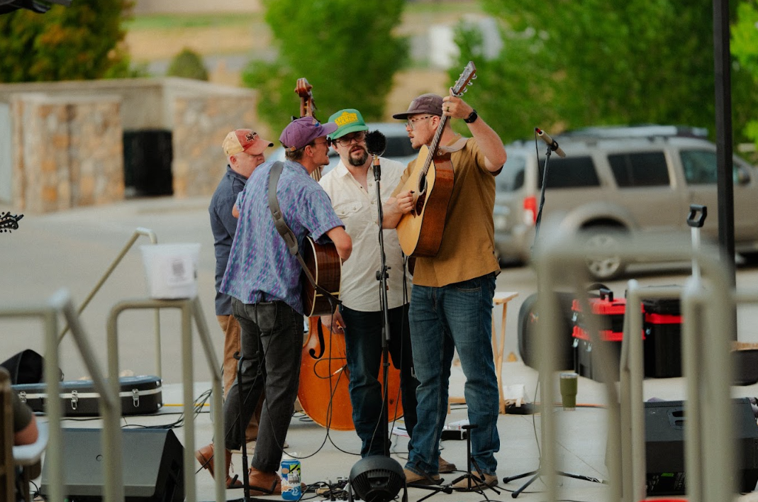 Group of four men performing music outdoors, with some playing guitars and microphones in front of them.