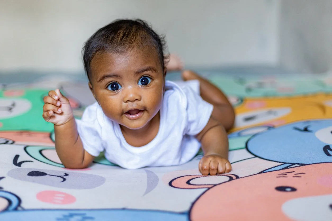 A baby with dark skin and short dark hair, lying on a colorful blanket, working on tolerating and enjoying tummy time during occupational therapy for infants in Metuchen, NJ