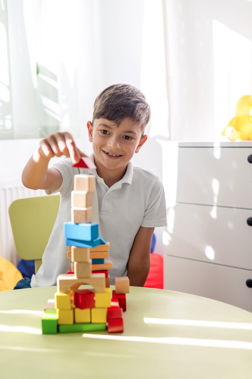 A young boy stacking colorful wooden blocks on a table in a bright room, working on fine motor skills during occupational therapy for children in Metuchen, NJ