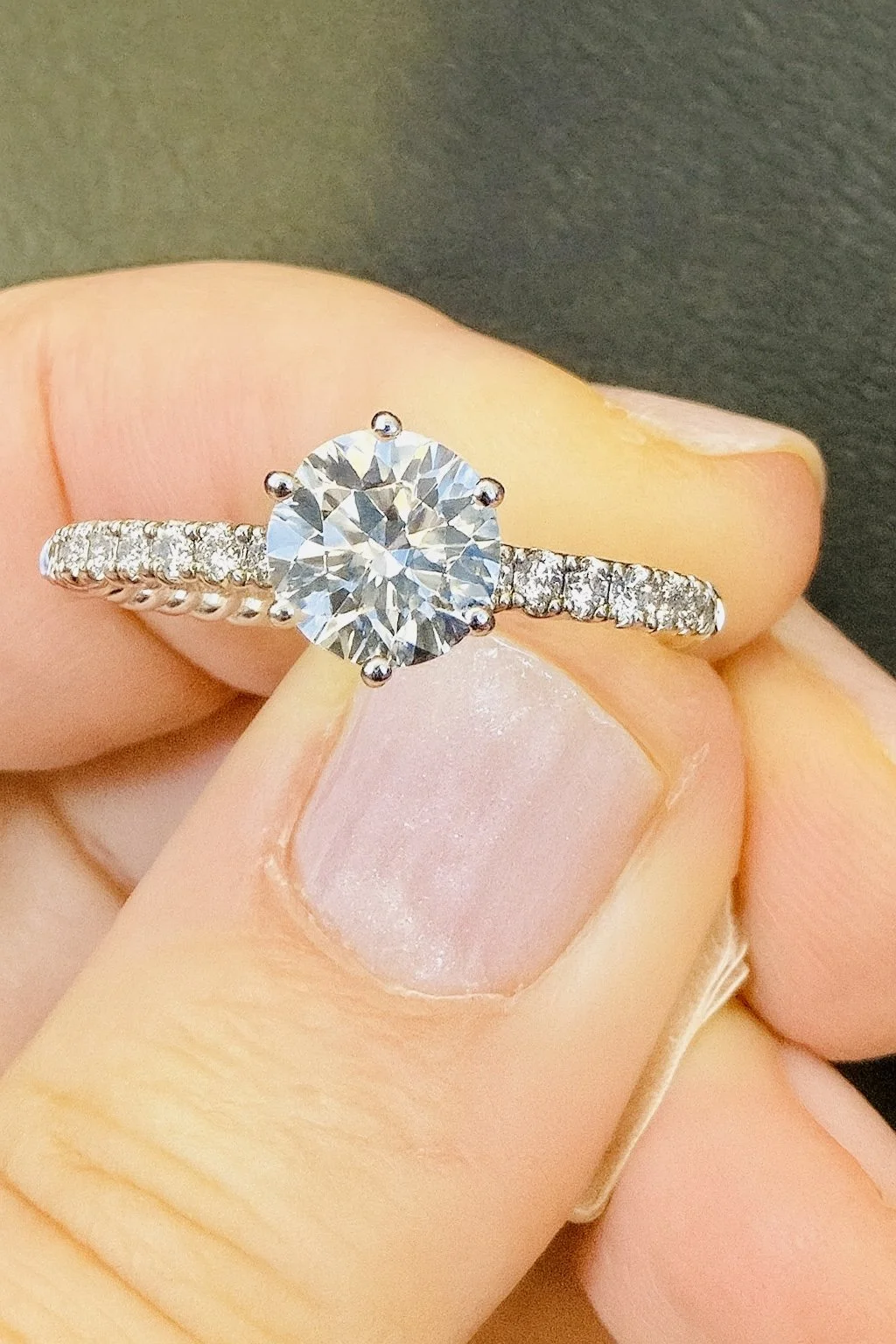 Round brilliant diamond engagement ring held in hand, showcasing the Engagement Ring Center at SINO Fine Jewelry in Boca Raton.