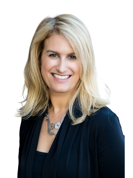 A woman with blonde hair smiling, wearing a black top and a navy blazer, with a silver necklace, against a plain background.