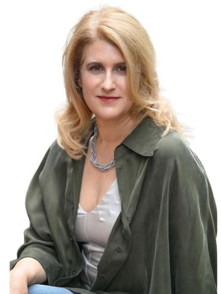 A woman with blonde hair smiling, wearing a black top and a navy blazer, with a silver necklace, against a plain background.