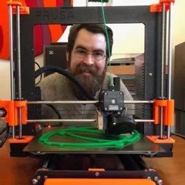 A man with glasses and a beard operating a 3D printer.