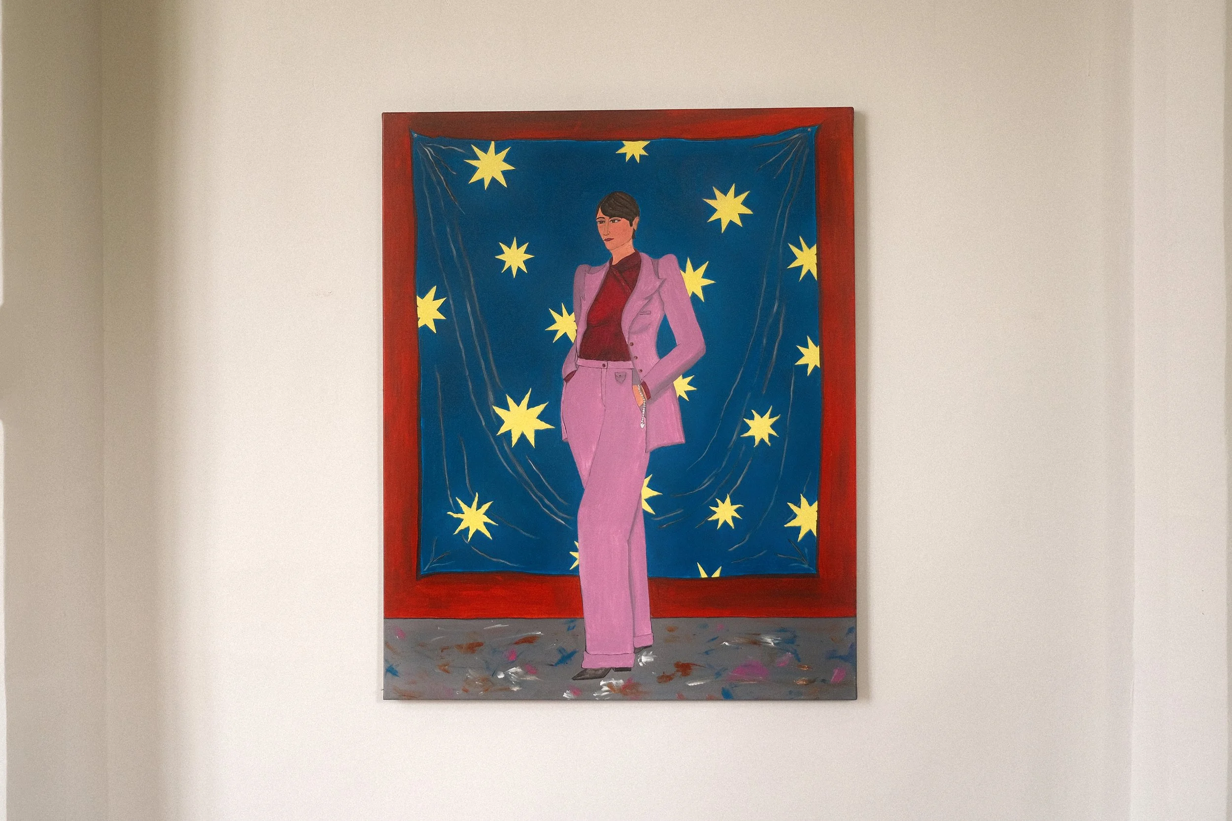 Mother and her lucky charm.
Figurative acrylic painting by Lola Nova.  A colorful painting featuring her mother in a powerful pose wearing a pink suit standing in front of a blue background with yellow stars, holding a silver necklace.