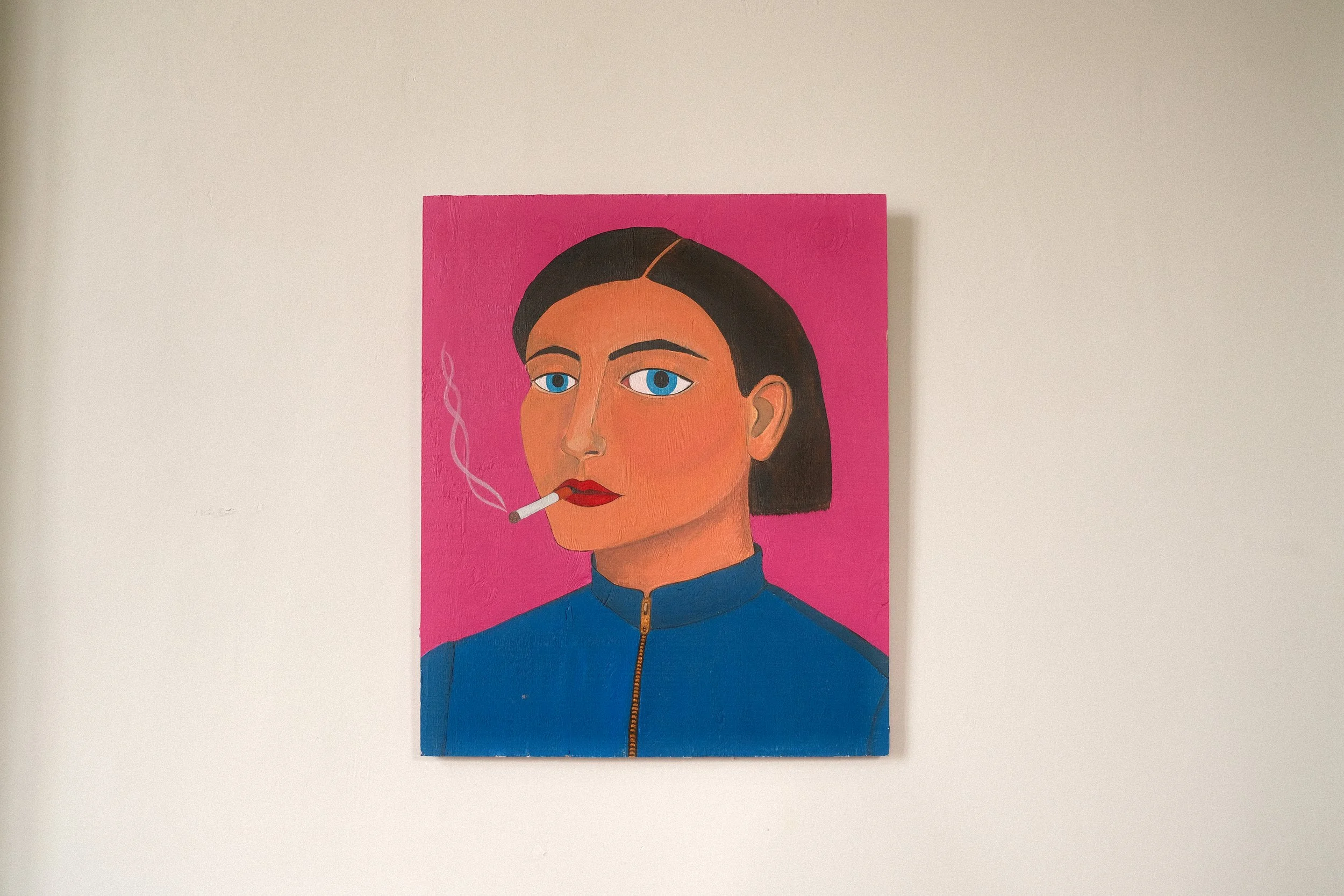 I used to smoke.
Figurative self-portrait painted by Lola Nova. A woman with brown hair, blue eyes, bold red lips, smoking a cigarette, wearing a blue jacket with a gold zipper, against a pink background.