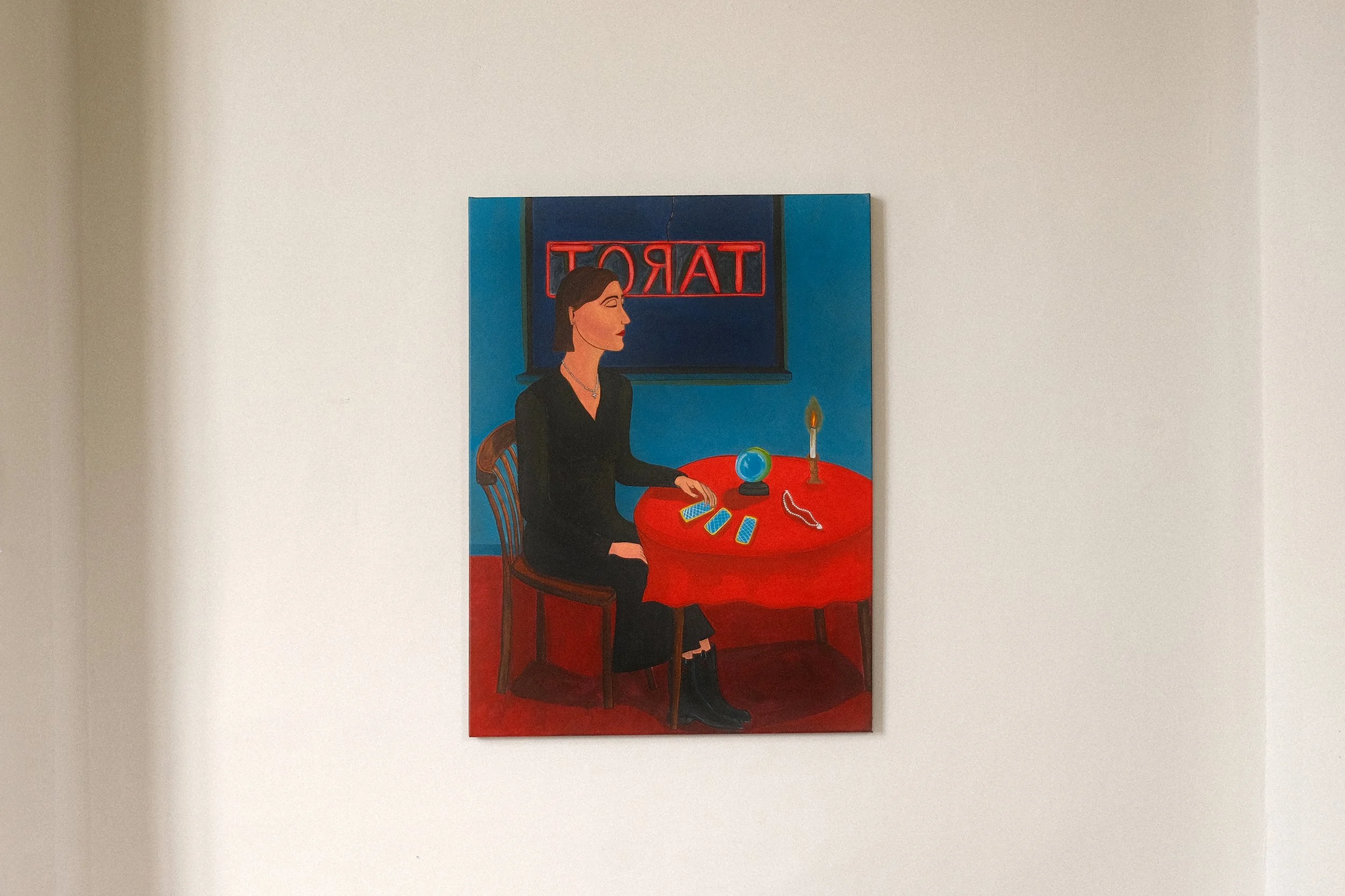 The Fortune teller.
Figurative acrylic painting by Lola Nova of her mother as a fortune teller sitting at a red table with Tarot cards, a crystal ball, a candle, and a necklace, in front of a window with a neon 'TAROT' sign.