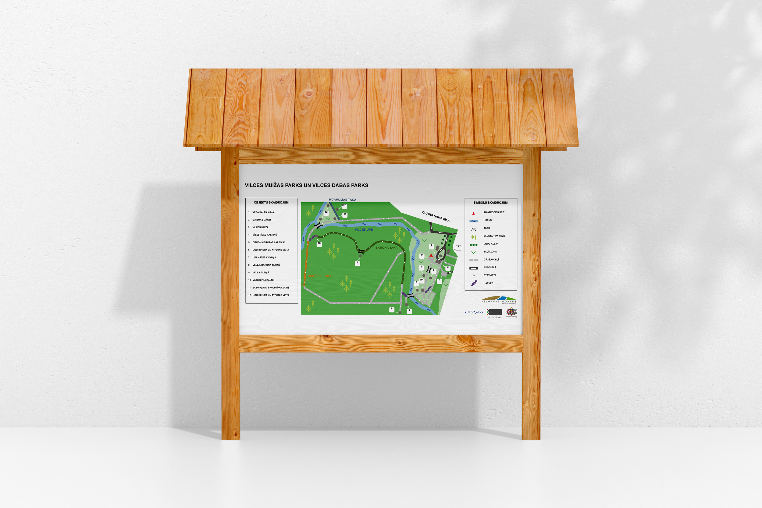 A detailed map of Vilces Muiza Park and Vilces Dabas Park mounted on a wooden stand, with a white wall in the background.