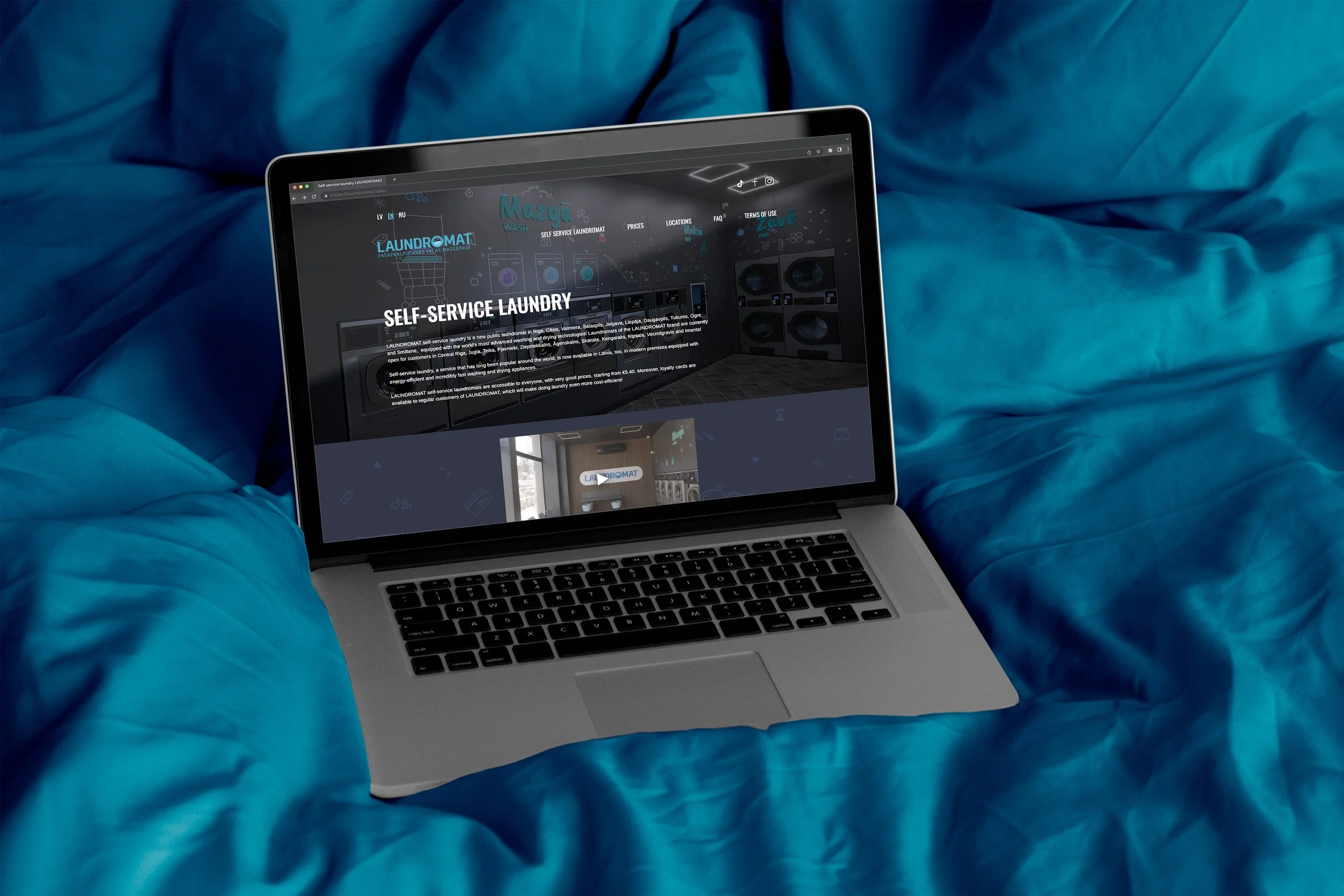 A laptop on a bed with blue sheets, displaying a webpage for a self-service laundry service.