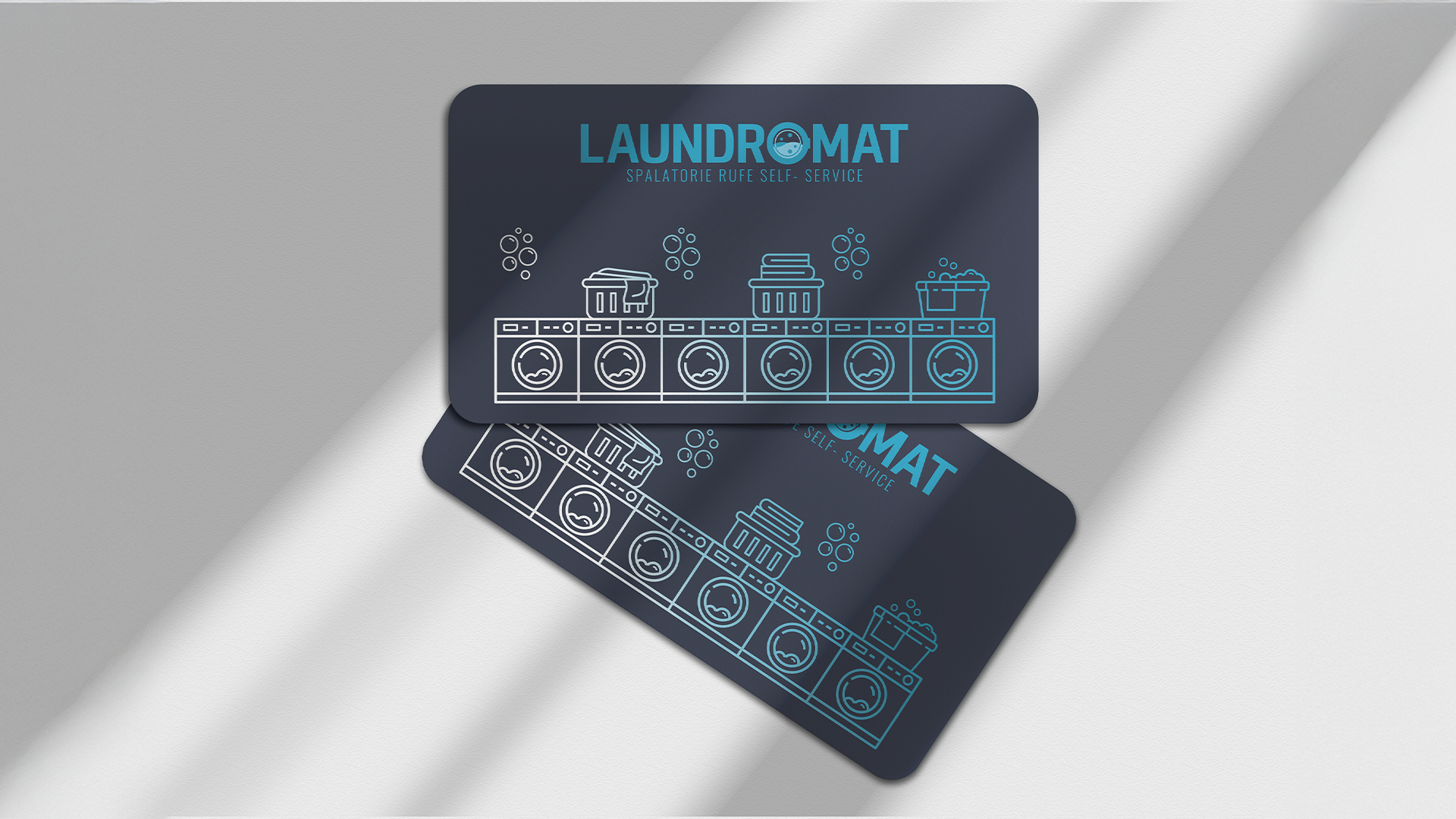 Two navy blue laundry cards featuring white and light blue line drawings of washing machines, laundry baskets, and bubbles. Text on the cards reads 'LAUNDROMAT' and 'SPALATORIE RUFE SELF-SERVICE.'